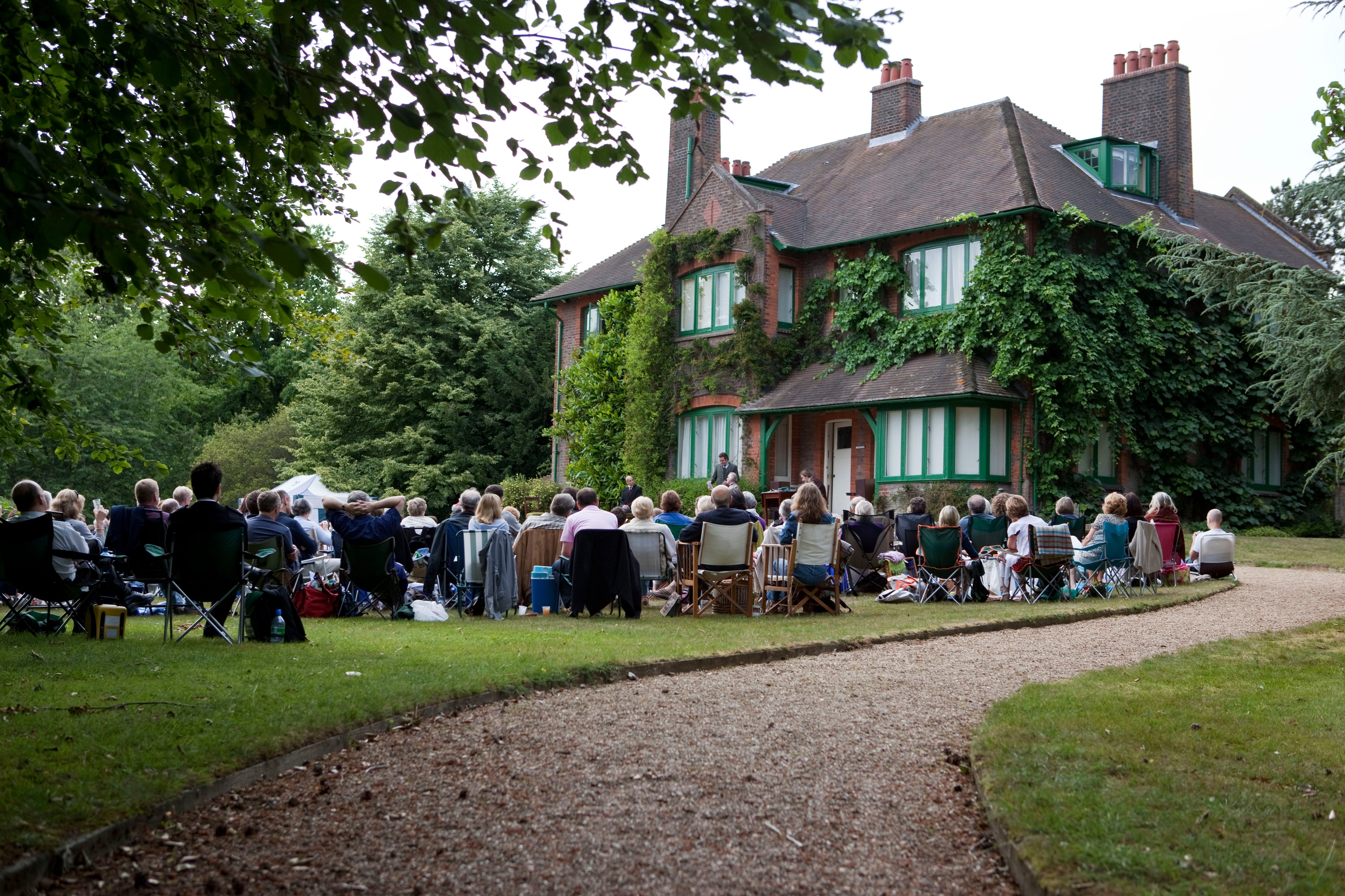 Audience at an outdoor theatre event with the house in the background at Shaw's Corner, Hertfordshire.