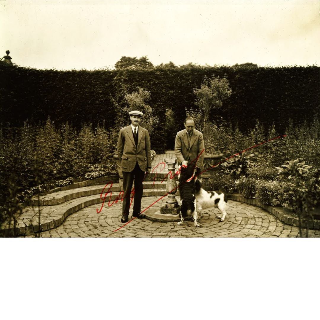 An archive photograph of two people standing in a garden, one with two dogs
