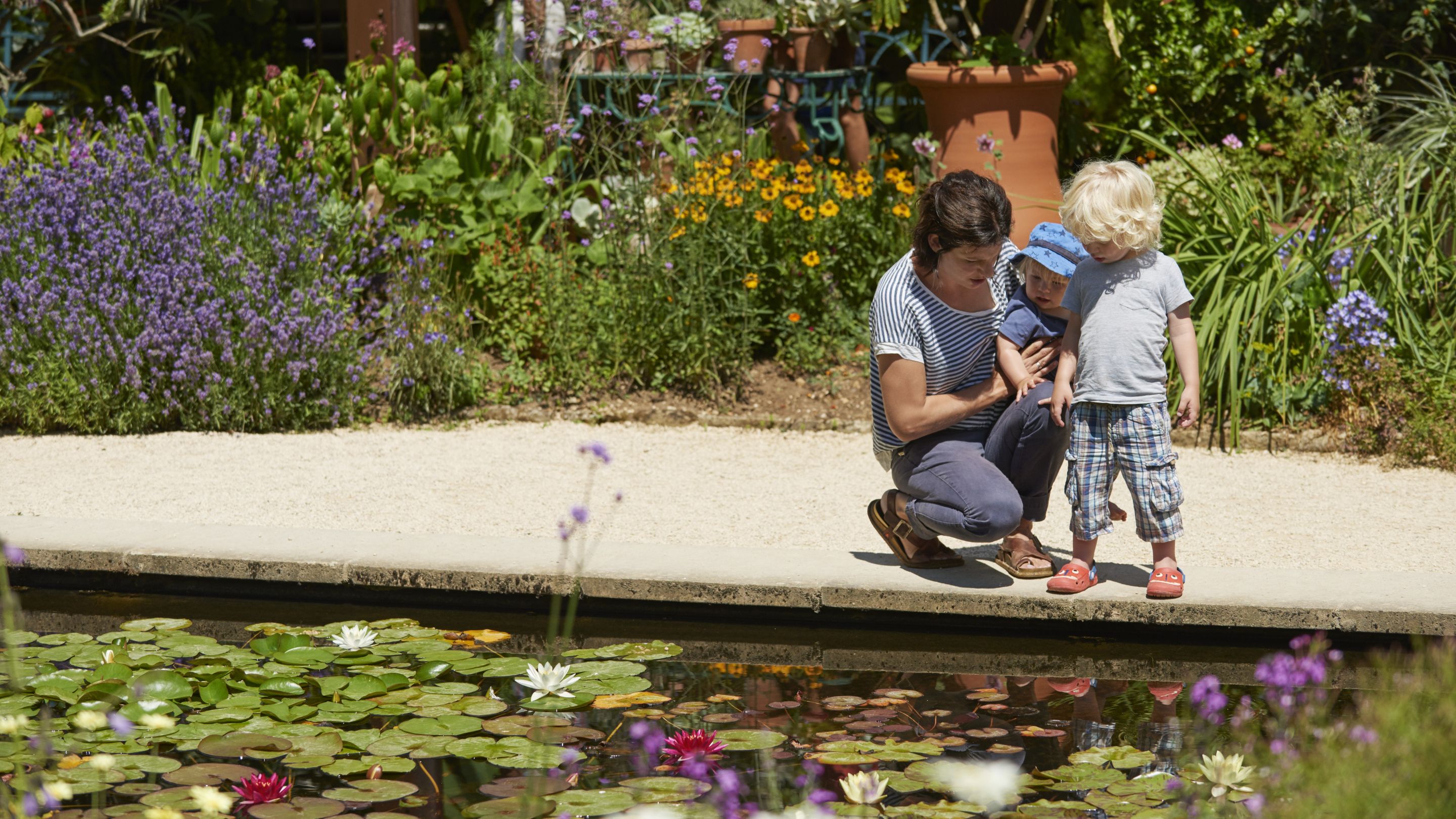 Mother and children kneeling by a lily pond at Hidcote, Gloucestershire