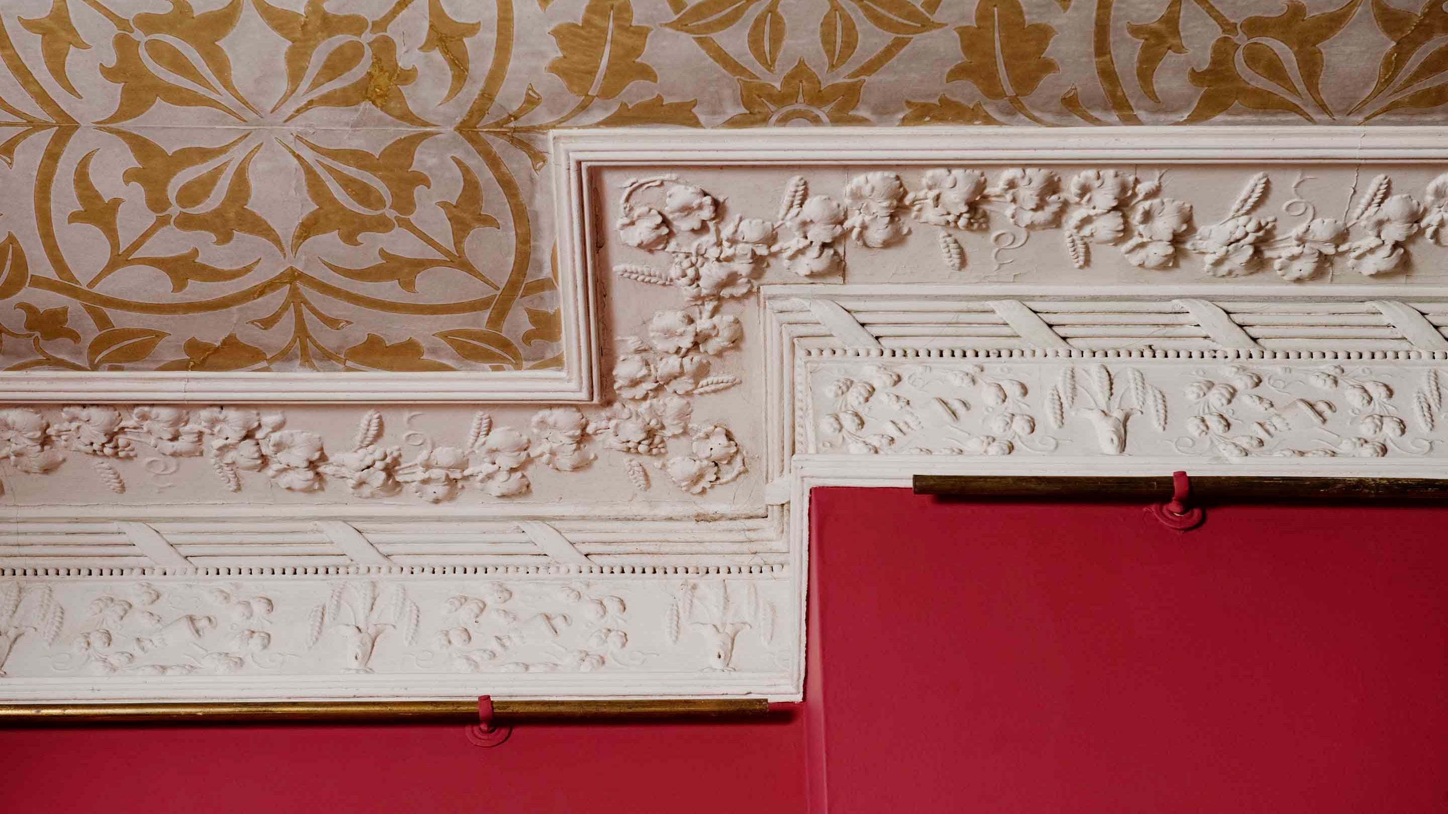 Yellow William Morris wallpaper against deep red wallpaper and white frieze at Newark Park
