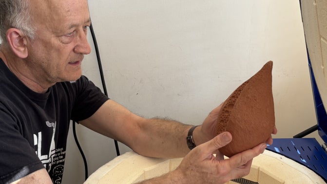 Man holding piece of fired ceramic by a kiln