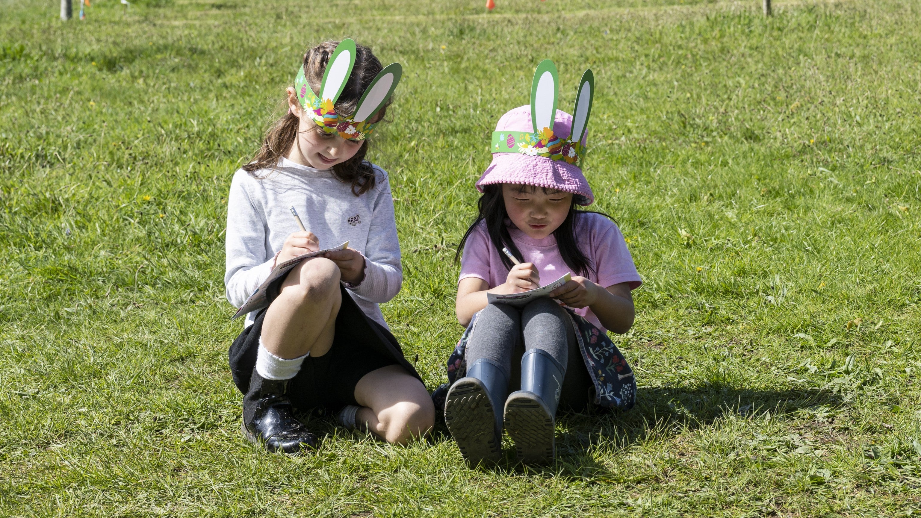Two girls in bunny ears sitting on a grassy bank