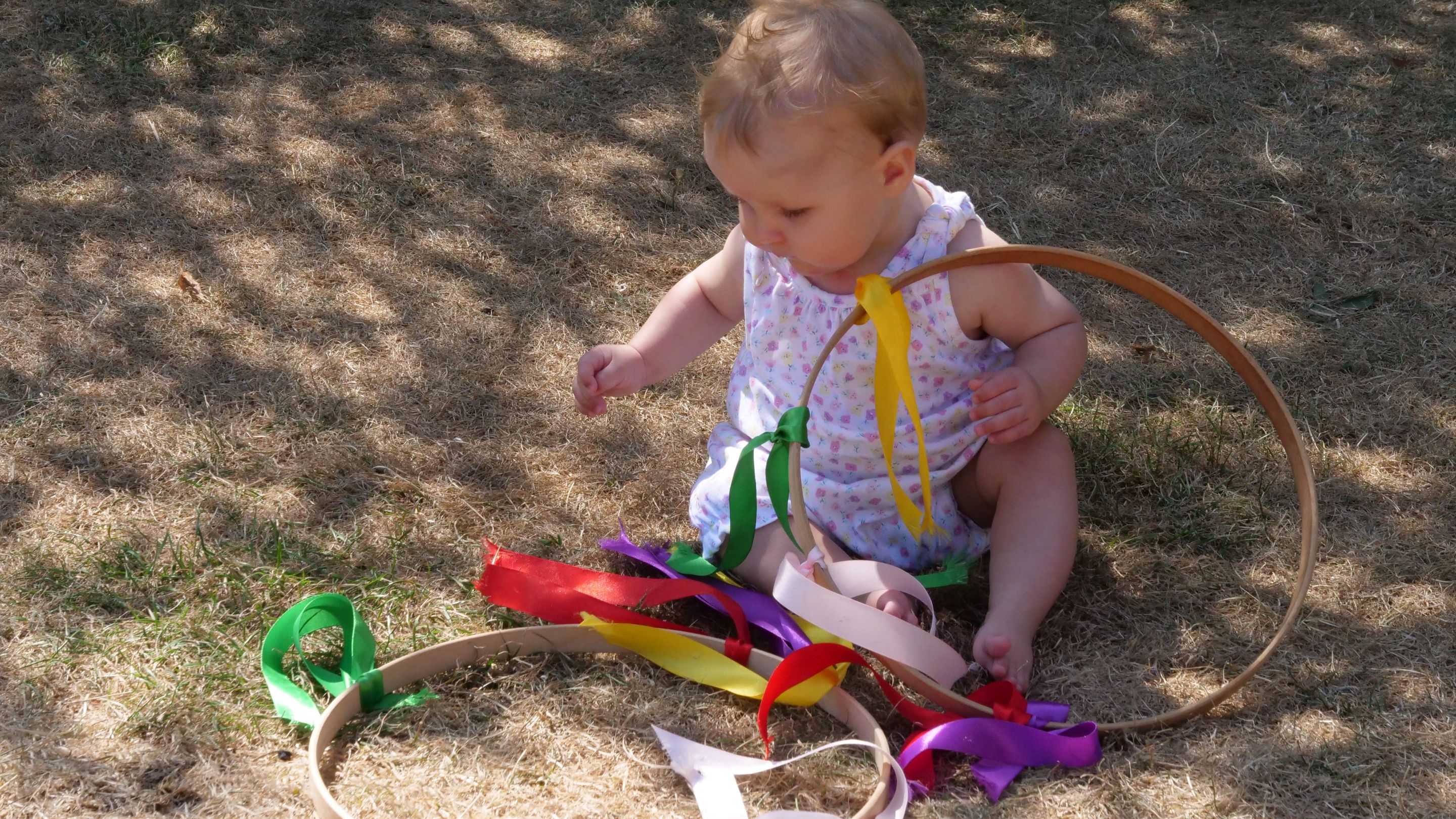 A small child sitting on the grass and playing with ribboned hoops