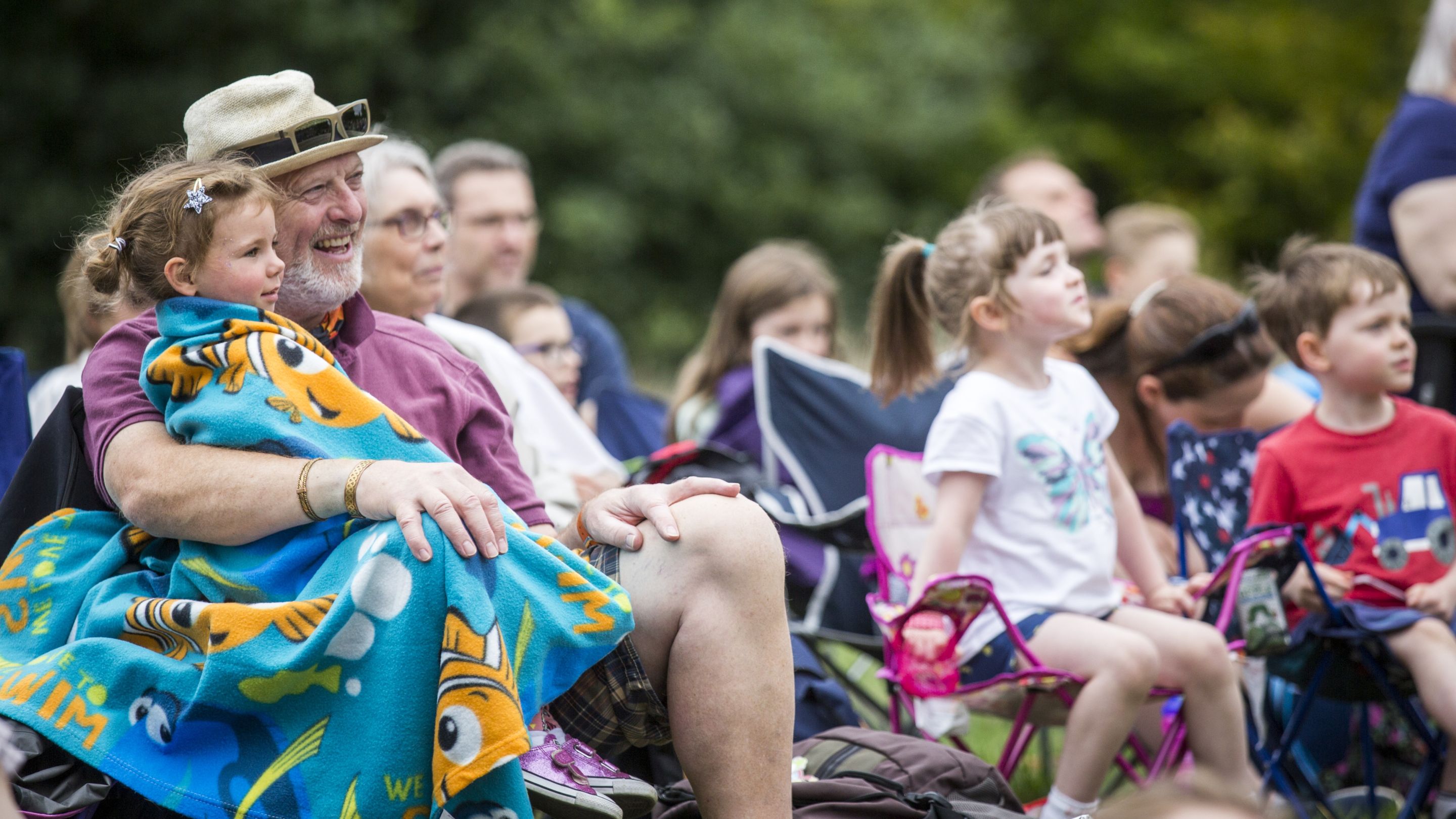 An audience enjoying an outdoor theatre event with an older man and young child in the foreground