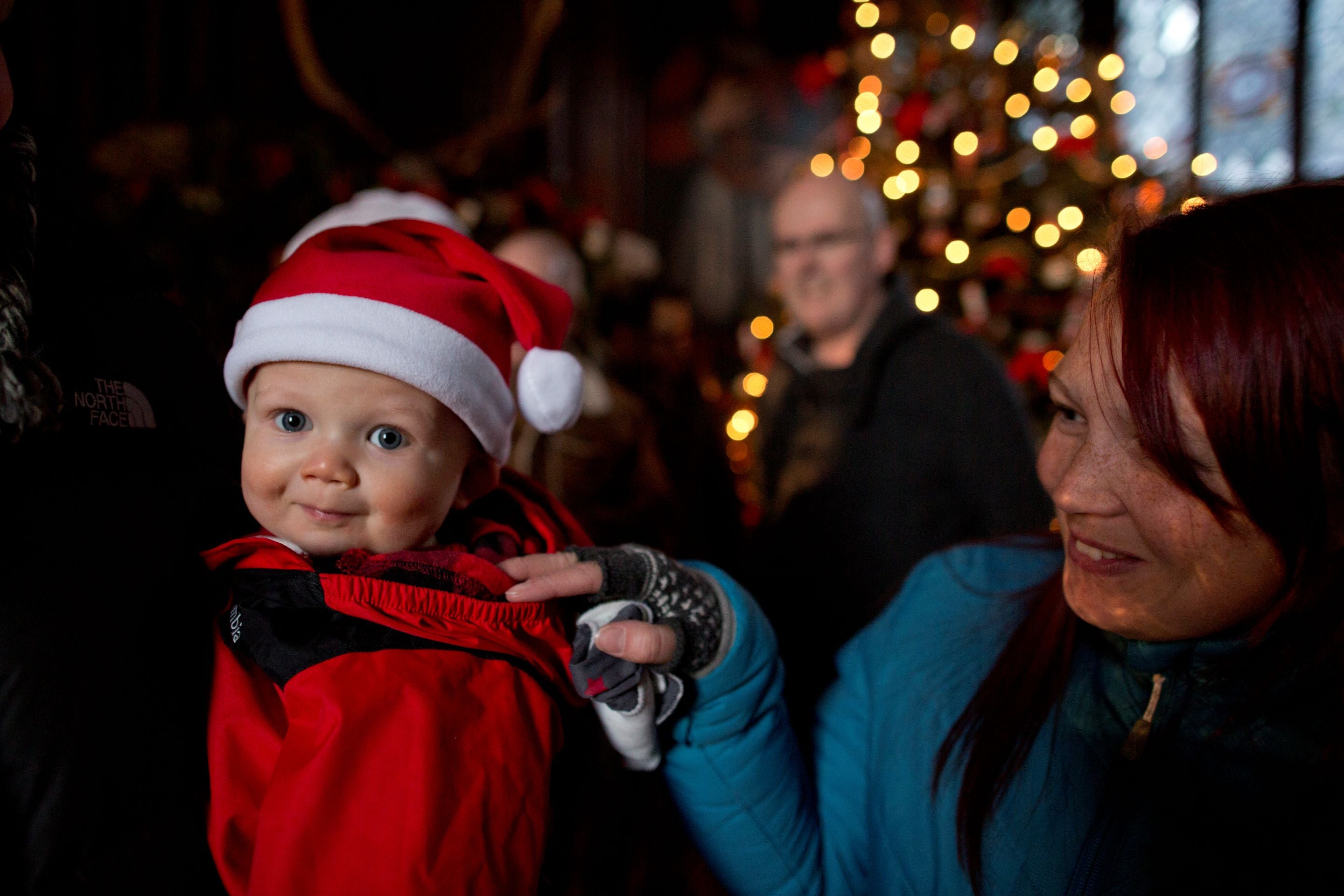 A small child in a Santa hat with their family and Christmas lights in the background