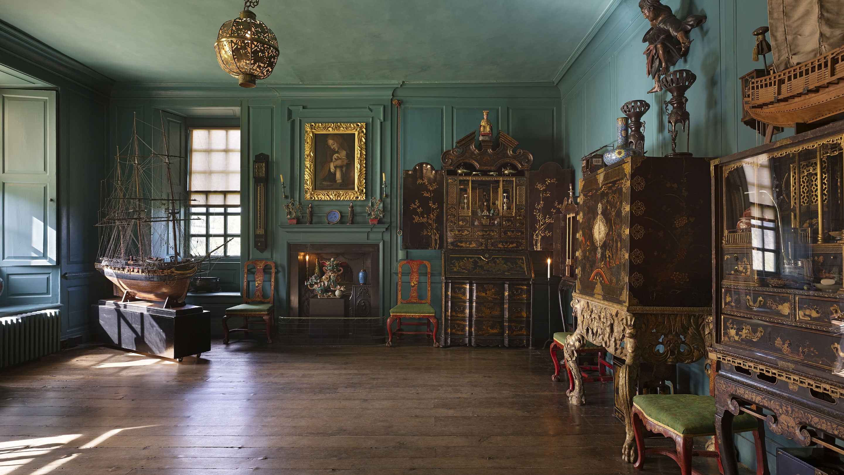 Interior shot of a panelled room, painted in a turquoise. Ornate display cabinets, built from dark woods and gold fixtures furnish the room, boldly contrasting with the colour of the walls.