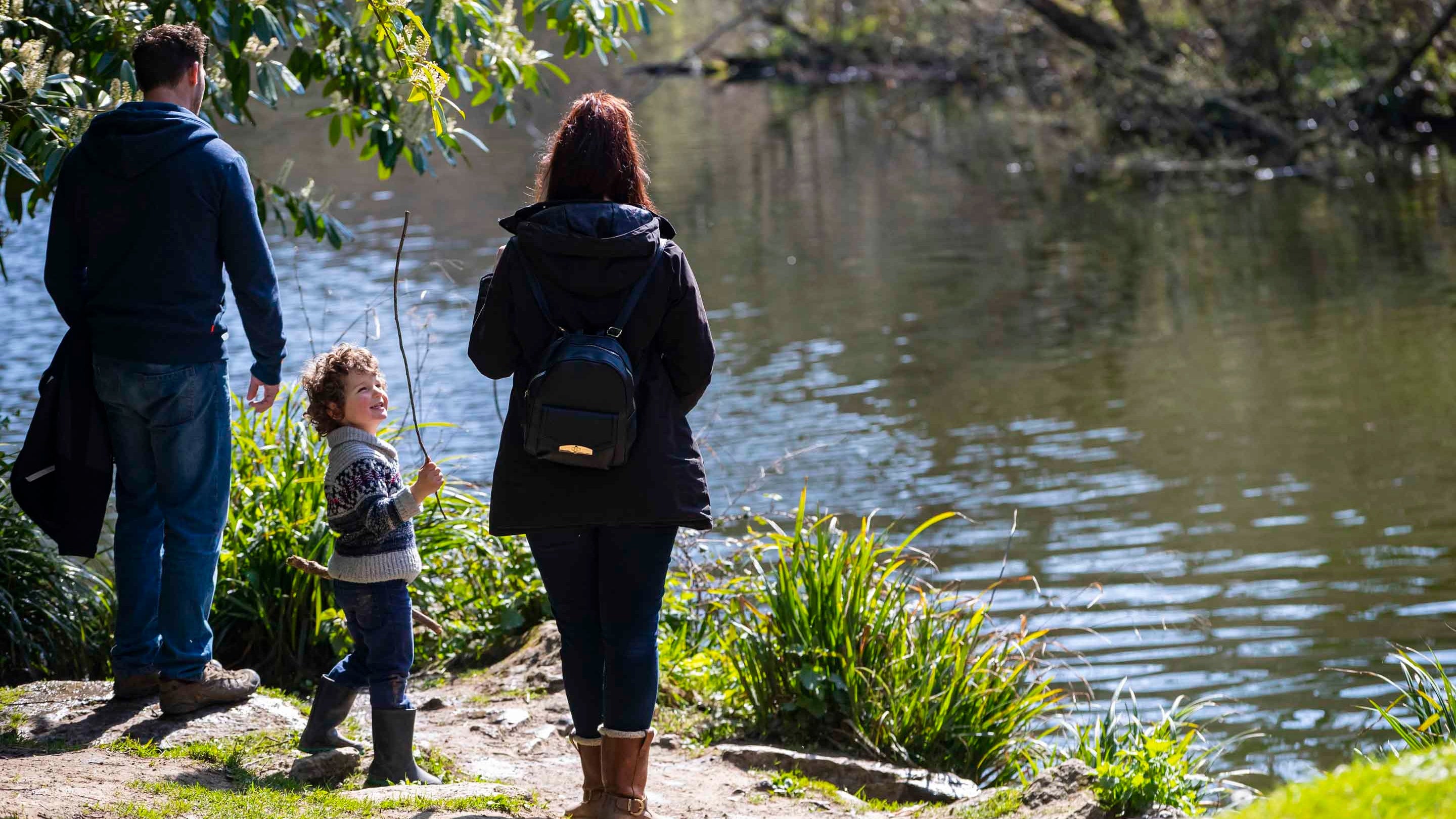 A family standing by the lake at Woodchester Park on a sunny day