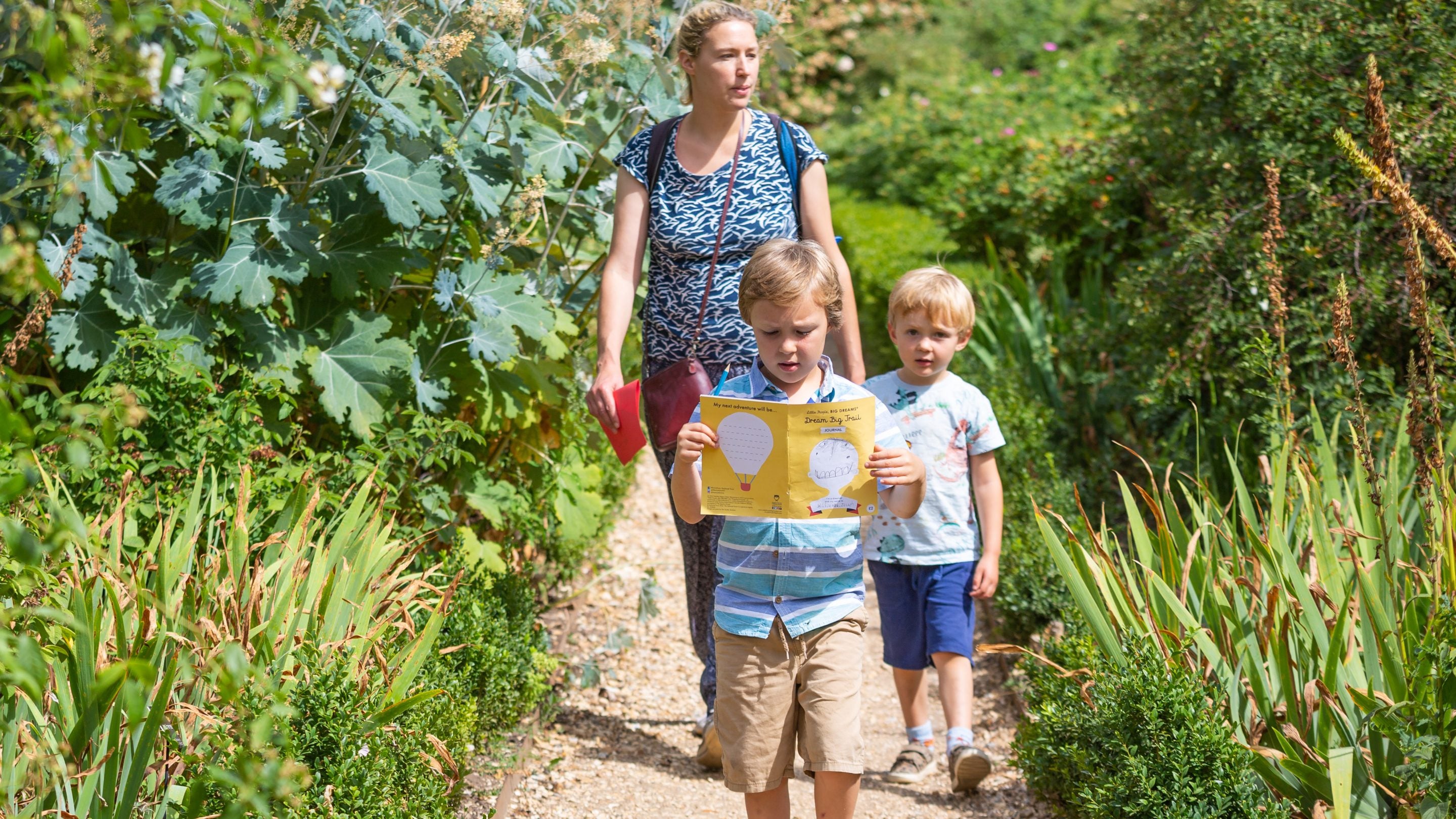 Family on a trail at Mottisfont. A young boy reading a trail booklet is leading his family along a garden footpath.