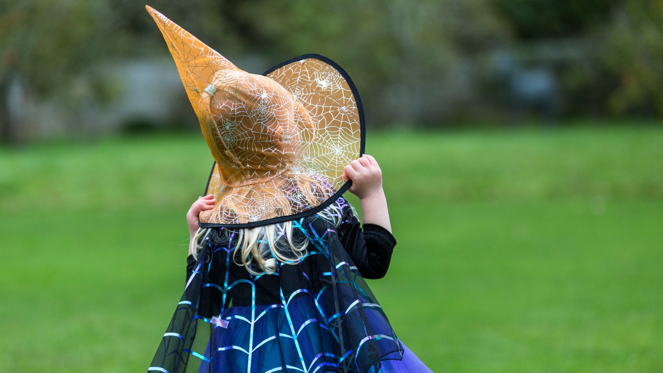 Back view of small girl in navy sparkly dress and gold witch's hat, on lawn, generic