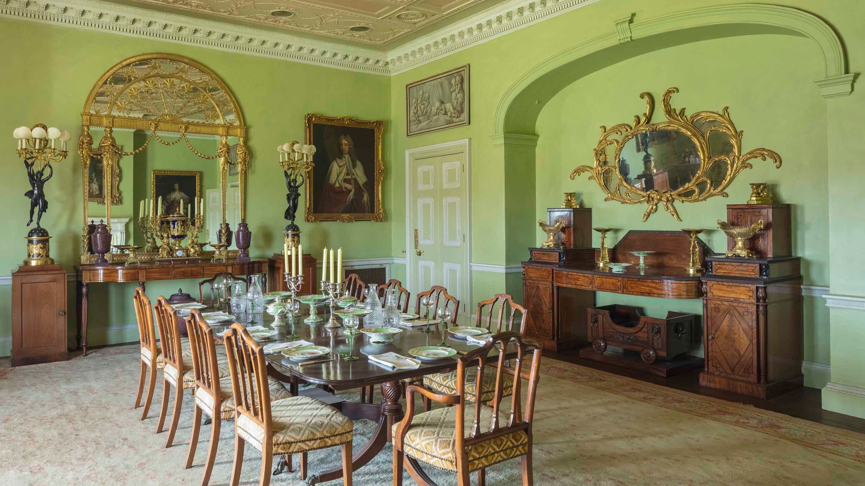 The Dining Room at Hinton Ampner, Hampshire, with 10 chairs around the table, in a pale green room with an intricately moulded ceiling