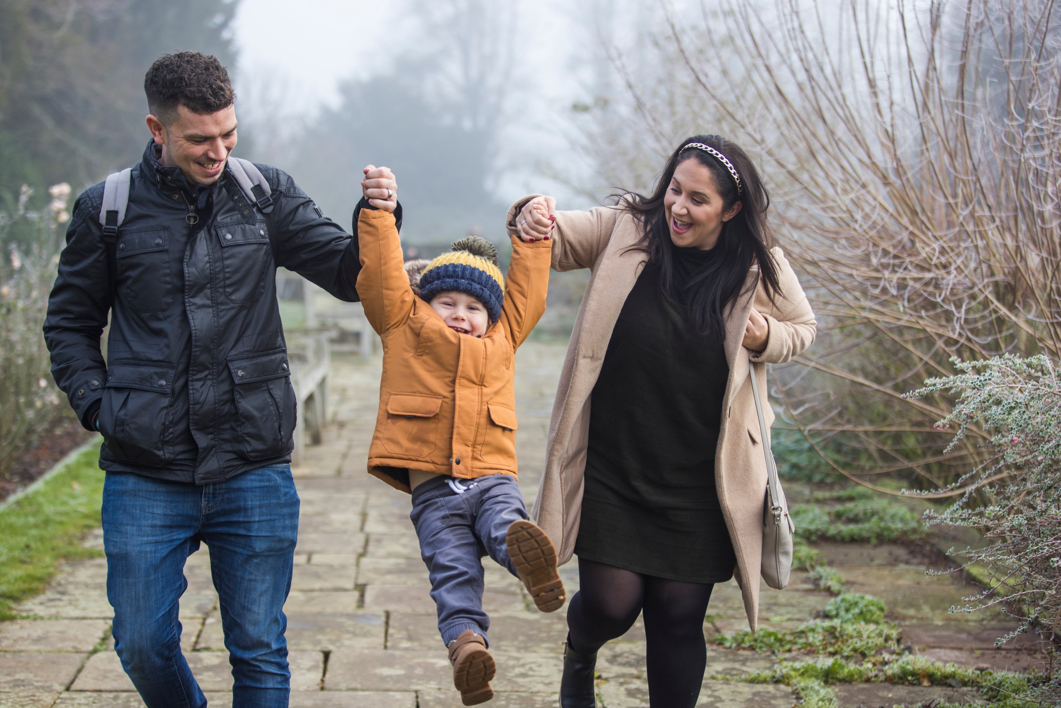 Two adults swing a child between them while walking along a garden path at Hinton Ampner in winter.
