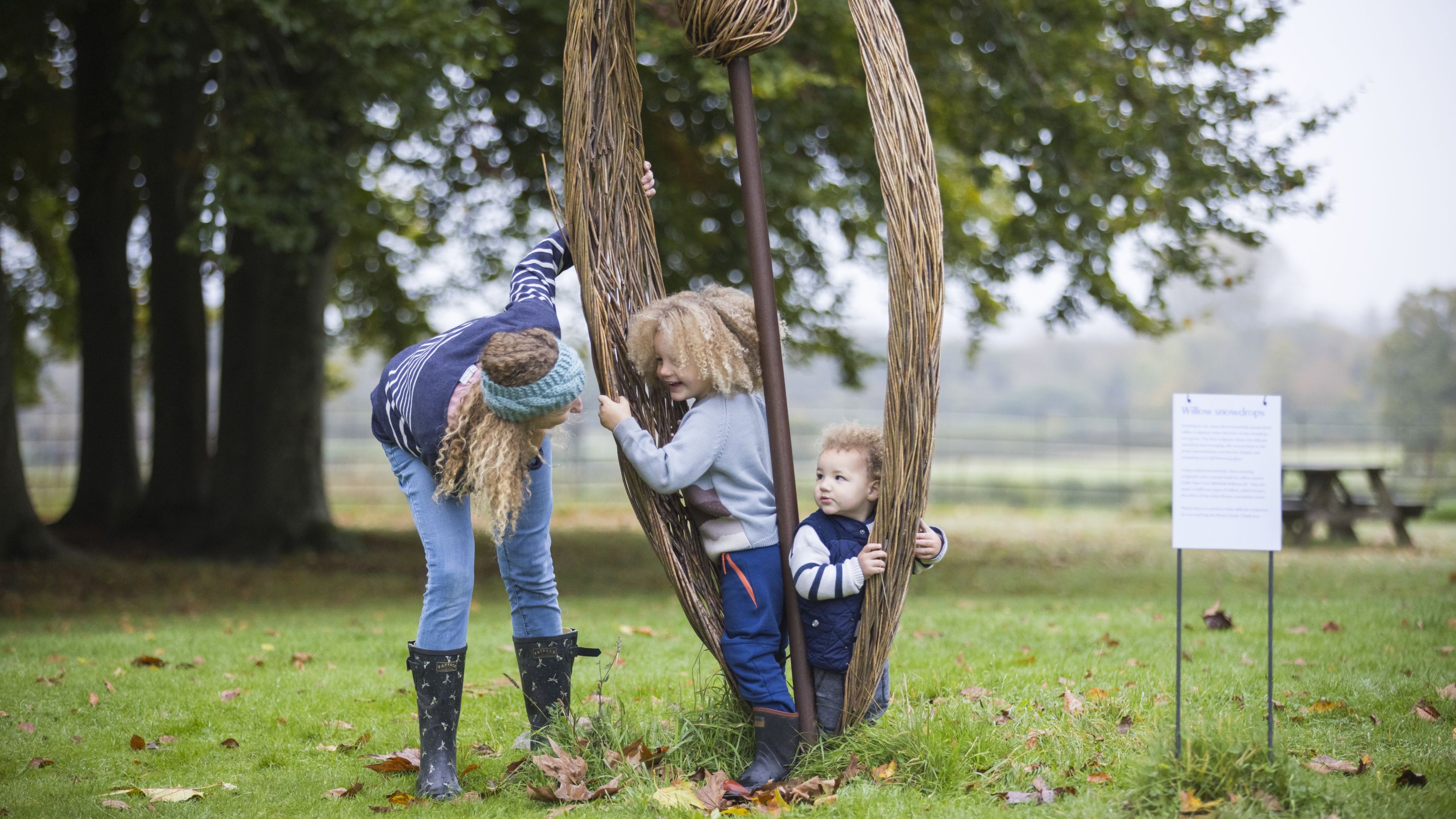 Two small children and an adult female exploring a giant willow sculpture in the garden at Mottisfont