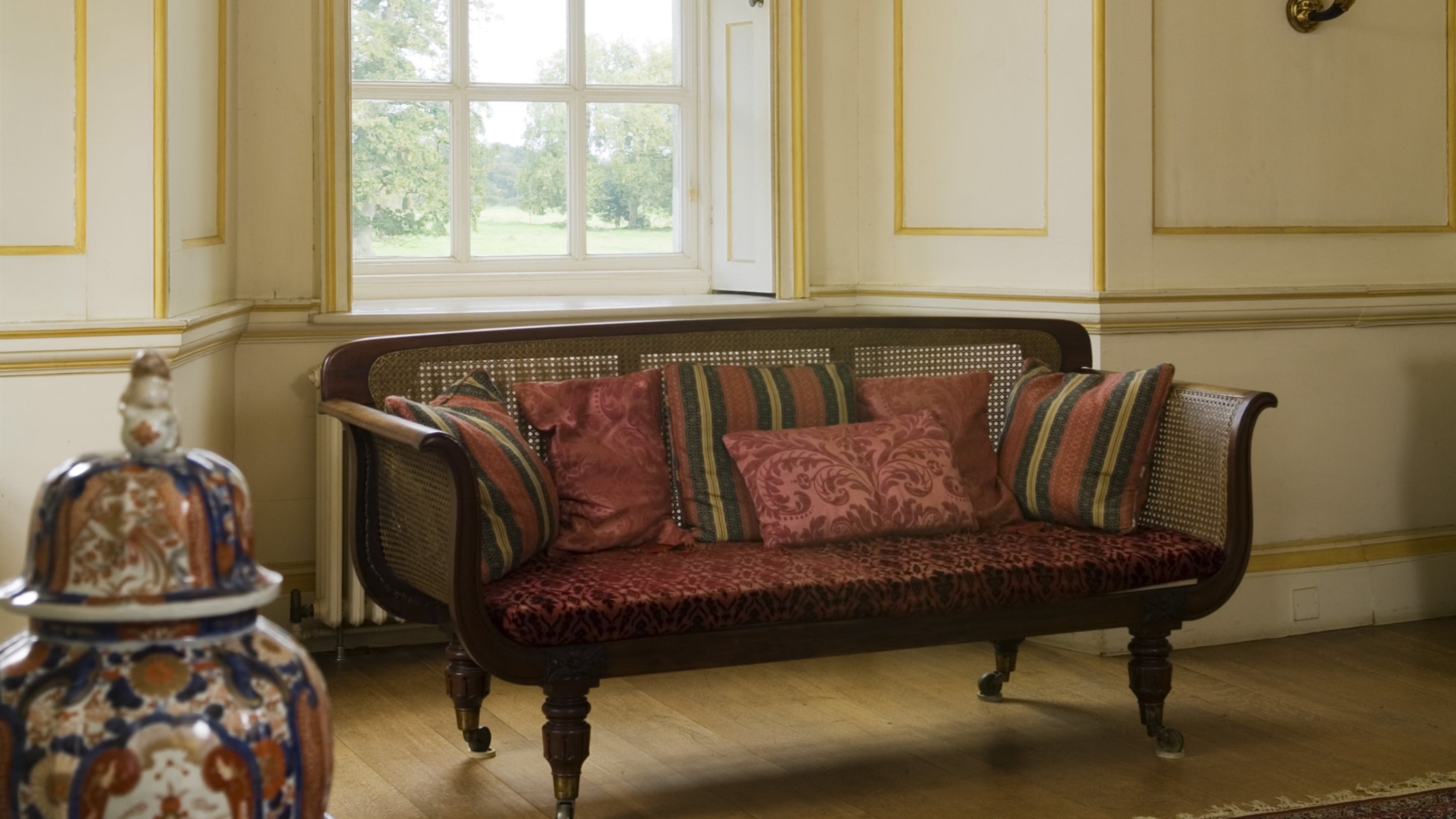 The cane-work sofa from Windsor Castle and eighteenth-century commode in the Entrance Hall at Mottisfont, Hampshire