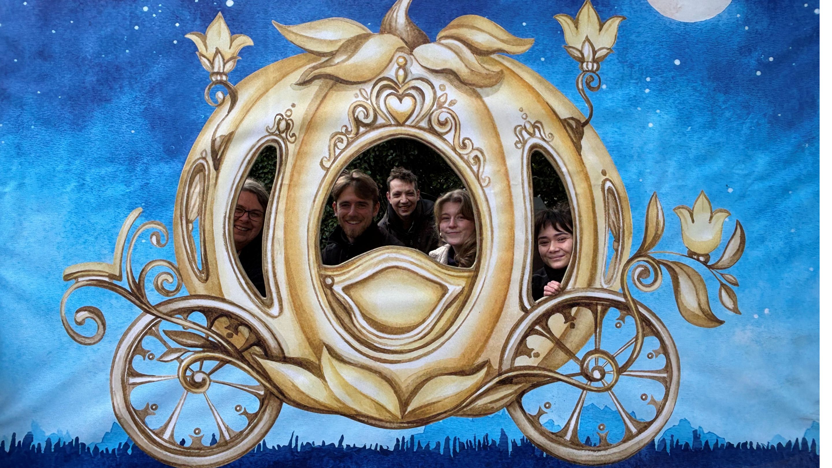 Staff peeping through the windows of a cut-out gold-coloured Cinderella carriage