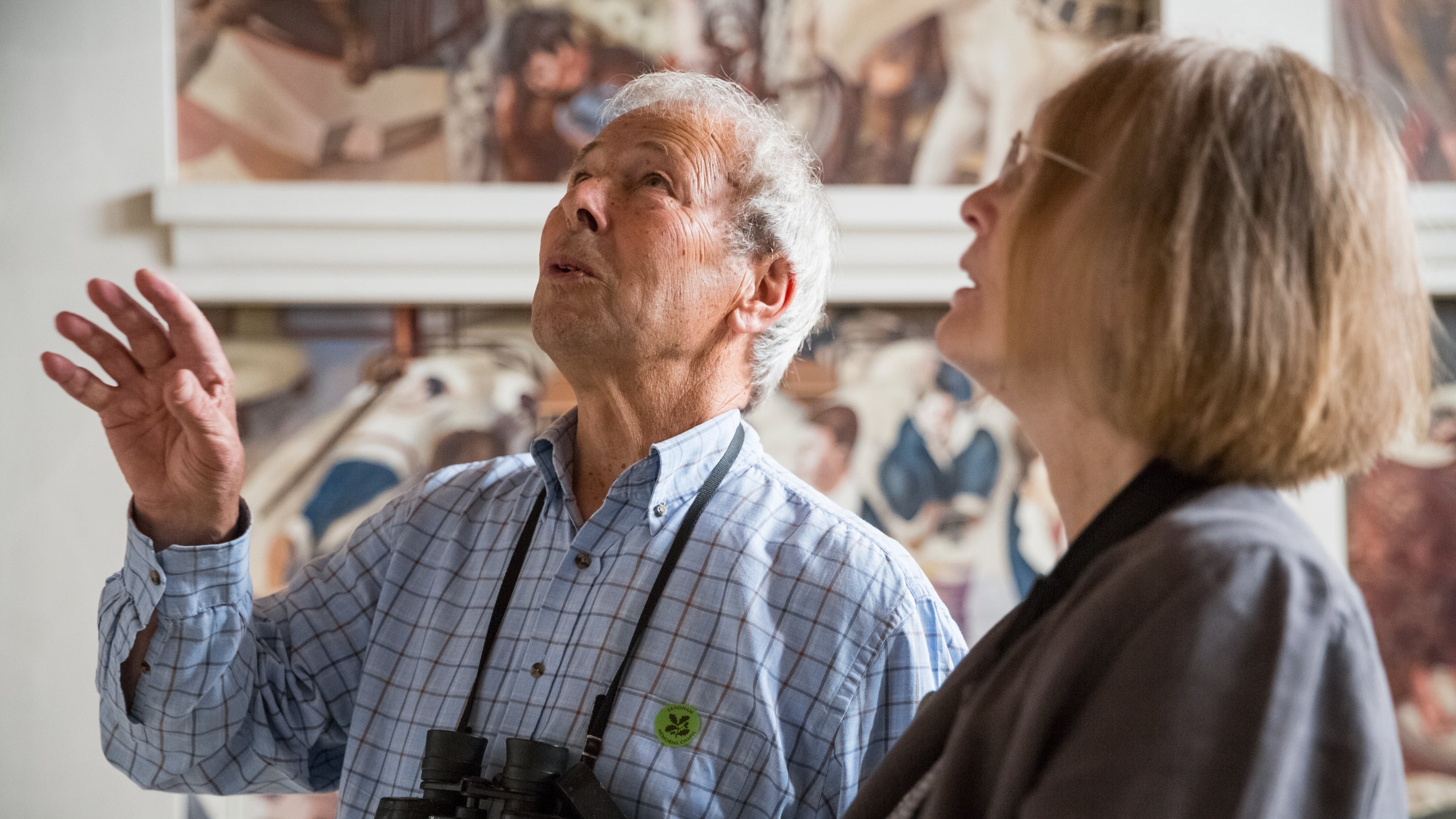 Two people in shallow focus look up at the paintings in Sandham Memorial Chapel