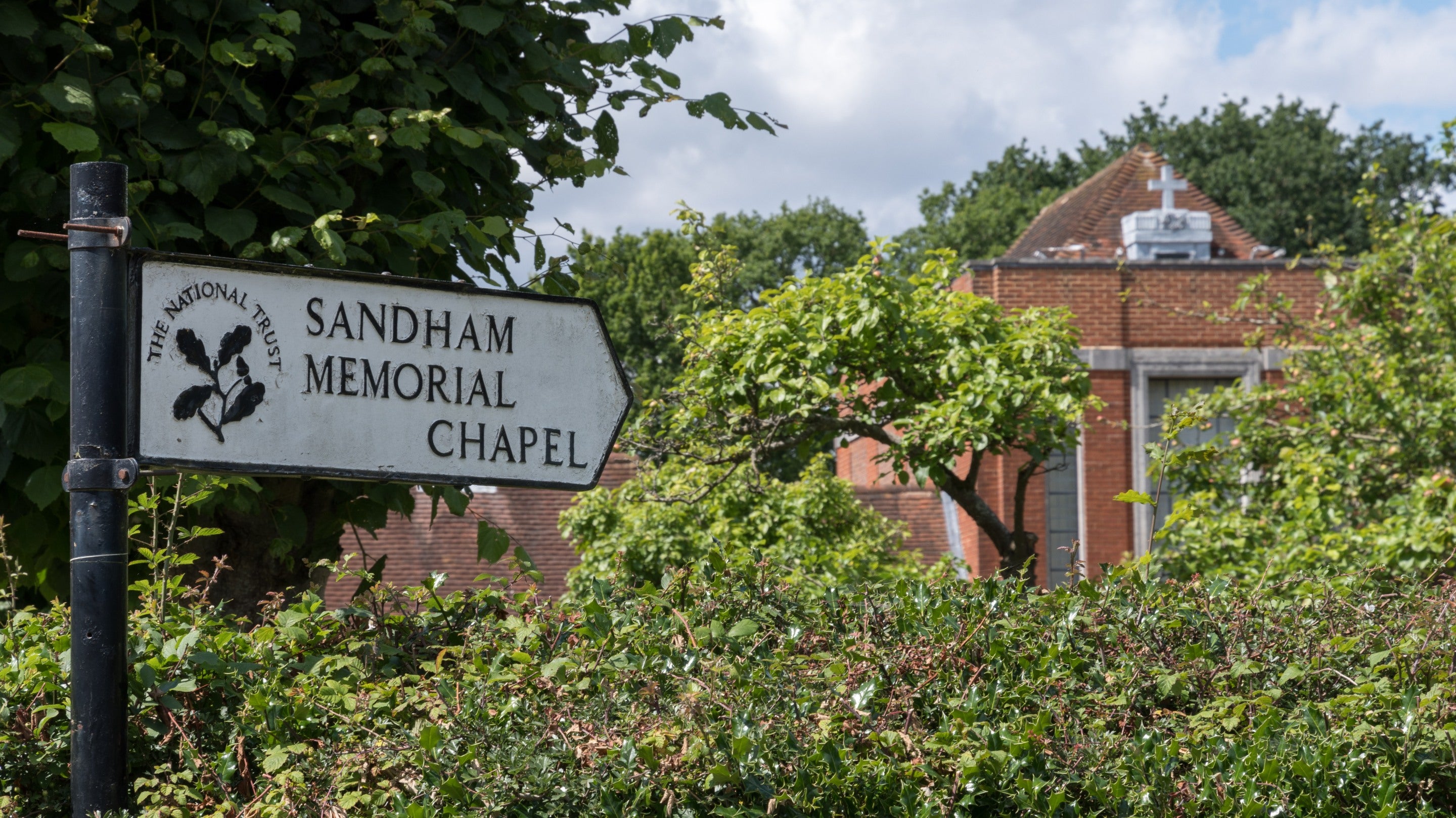 Signpost for Sandham Memorial Chapel, with the chapel behind slightly obscured by trees