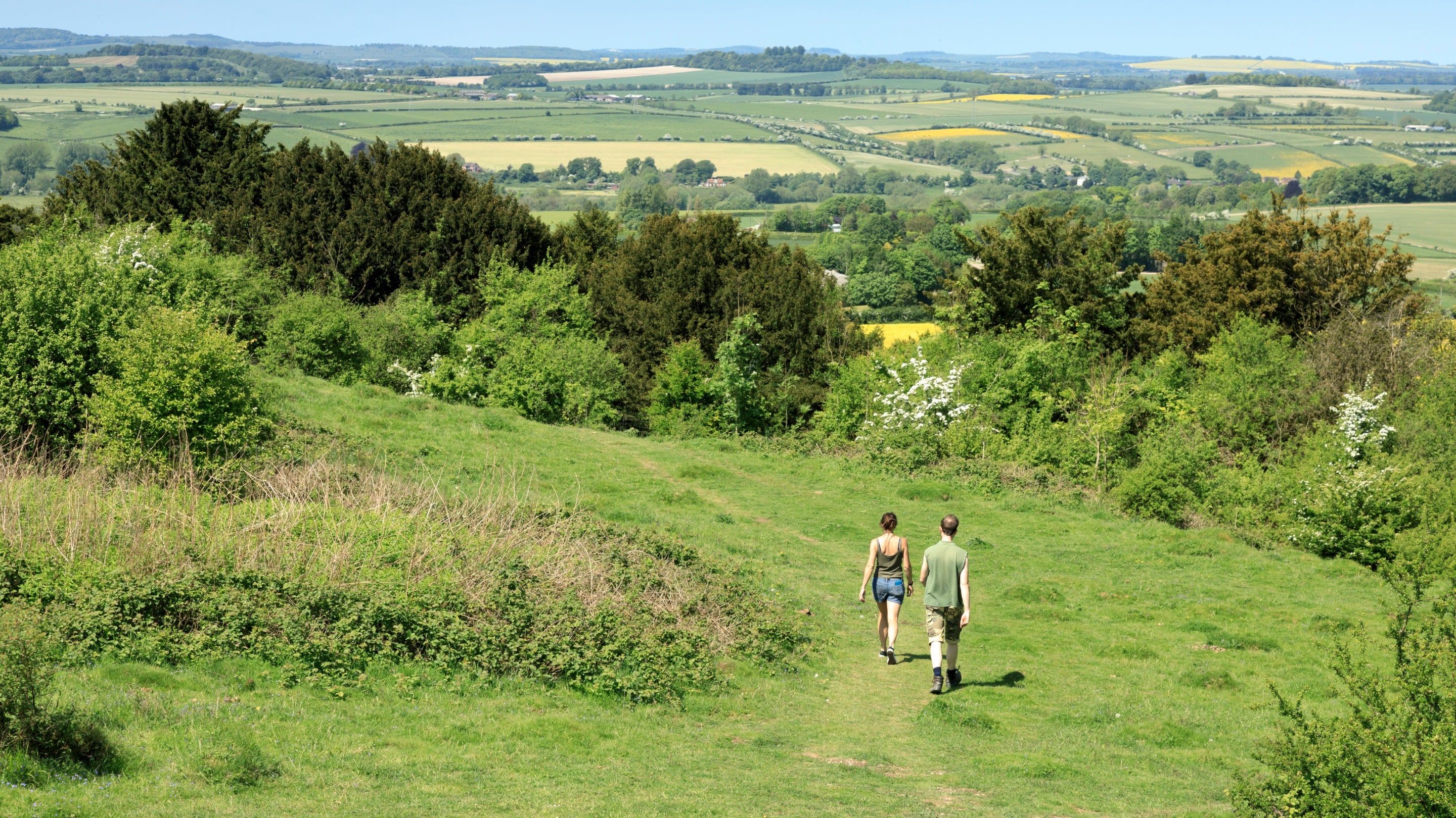 Two people walking along a grass path on Stockbridge Down, with views of the surrounding countryside