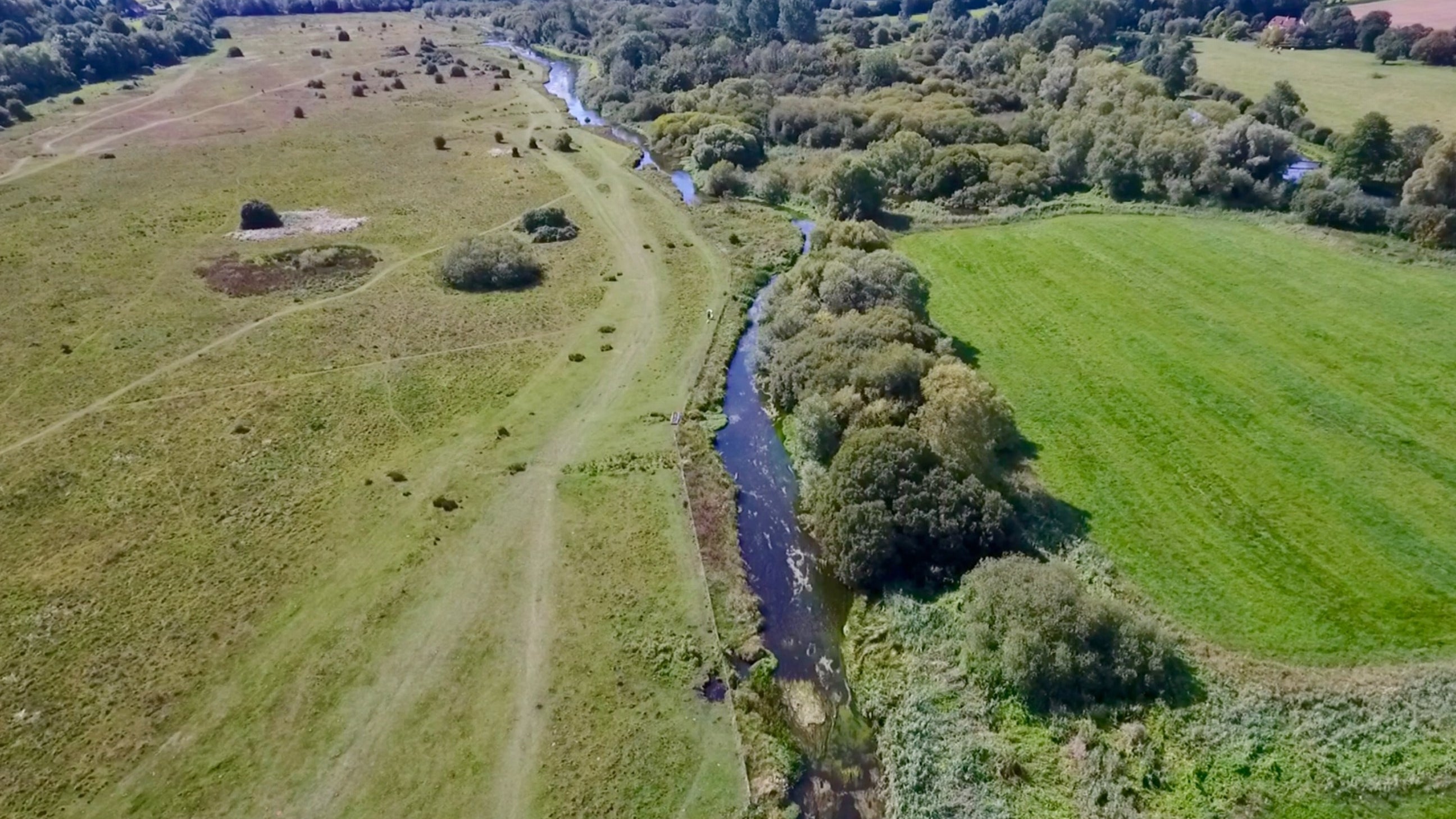 An aerial view of the tree-lined river and marshland in summer at Stockbridge Down, Hampshire