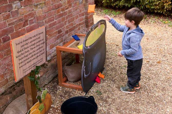 A young boy tosses bean bags into a cauldron.
