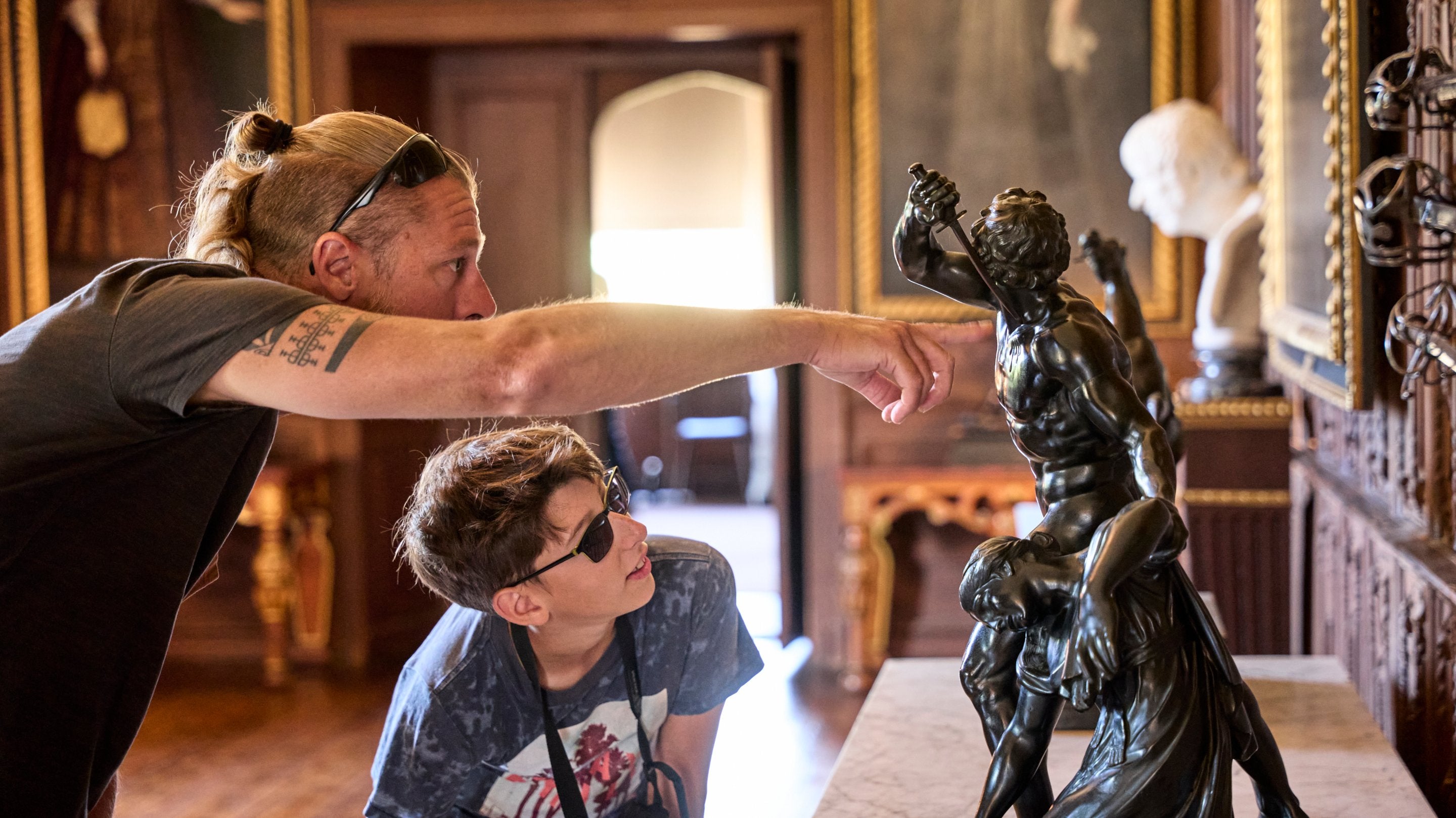 A father and son examine a classical sculpture on a table.