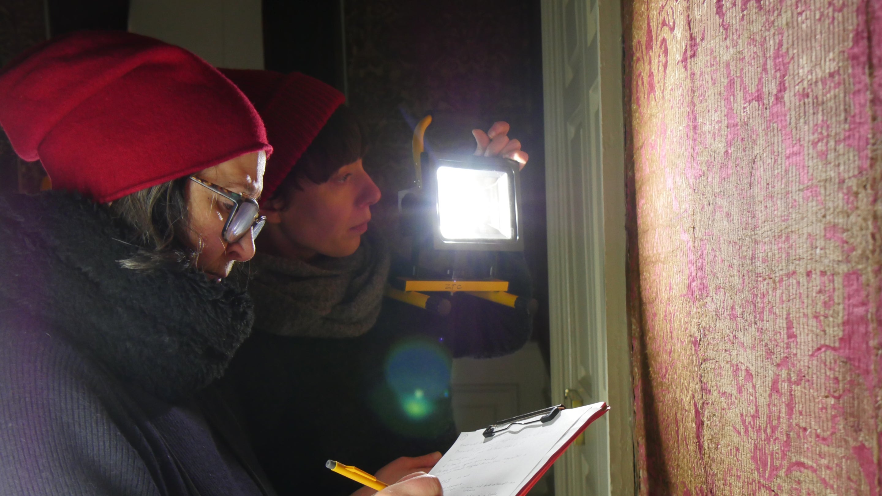 Two conservators examine wall hangings at The Vyne.