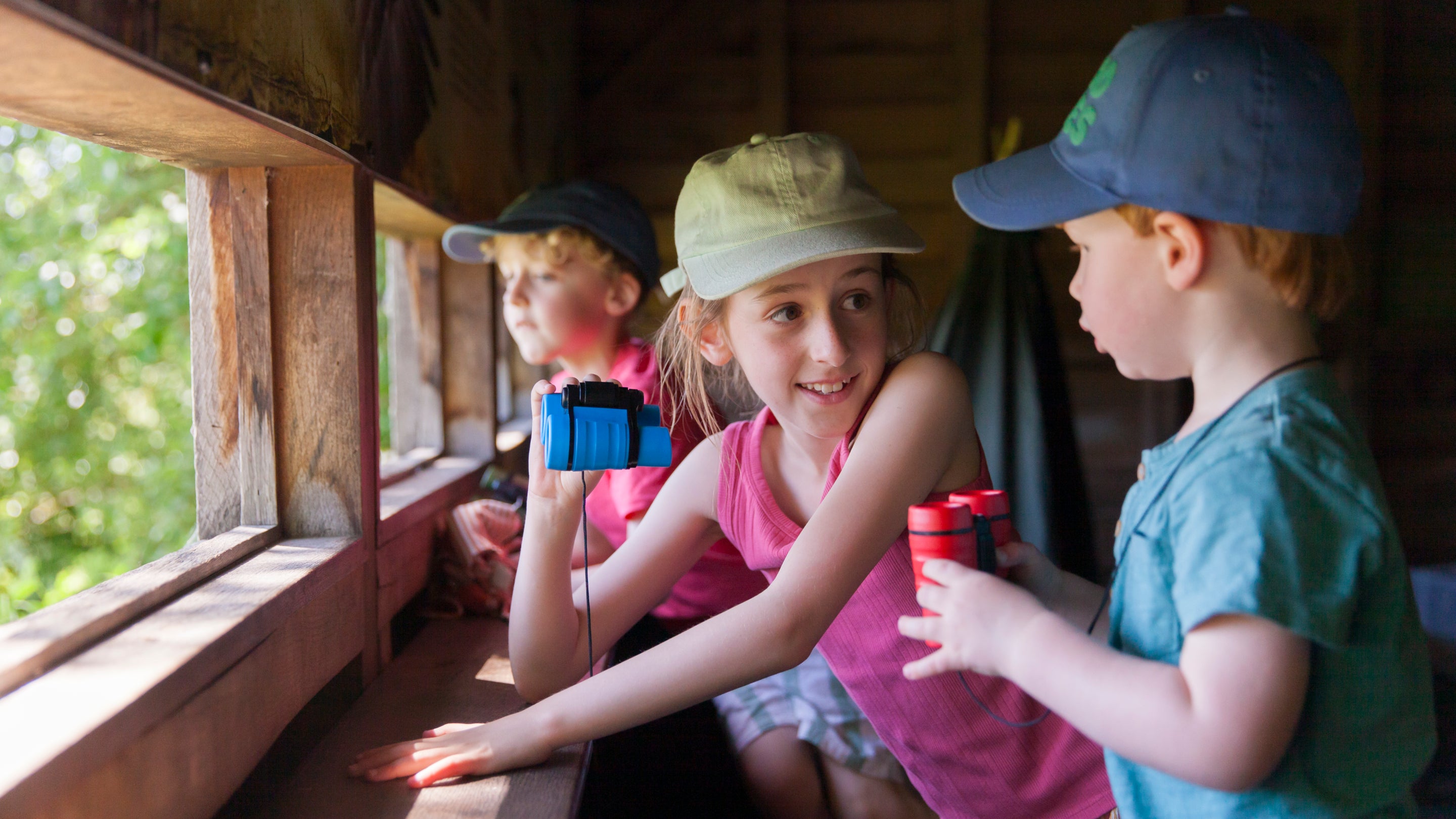 children sit in a bird hide holding binoculars.