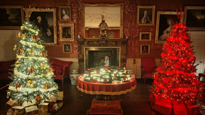 Christmas trees sit either side of an illuminated table of books and roses arranged in a tower and topped with a red rose in a bell jar.