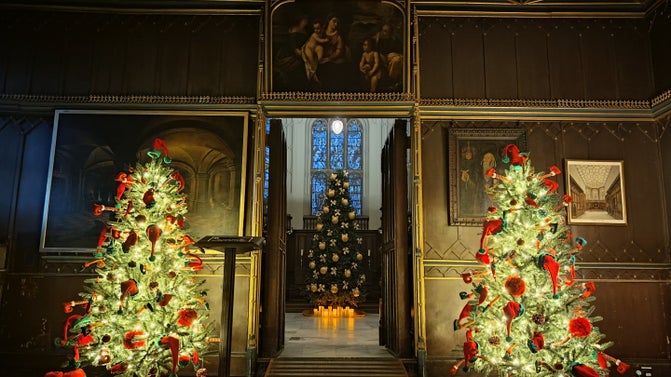 Christmas trees jauntily decorated with elf hats and shoes sit either side of the entrance to the chapel. In the distance, a large Christmas tree sits in the centre of the frame.