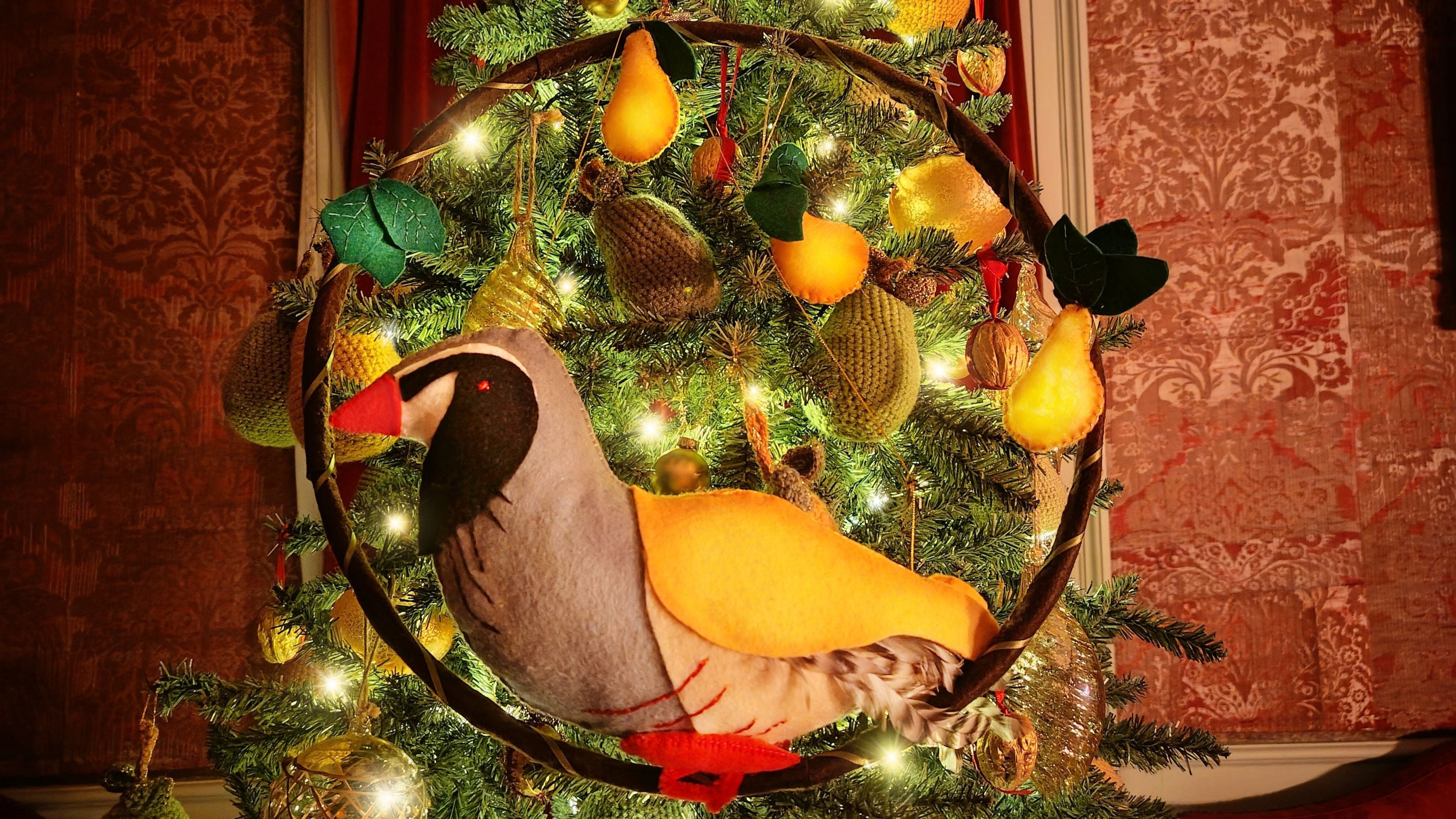 A textile bird sits in a Christmas tree surrounded by crochet and glass baubles and twinkly lights.