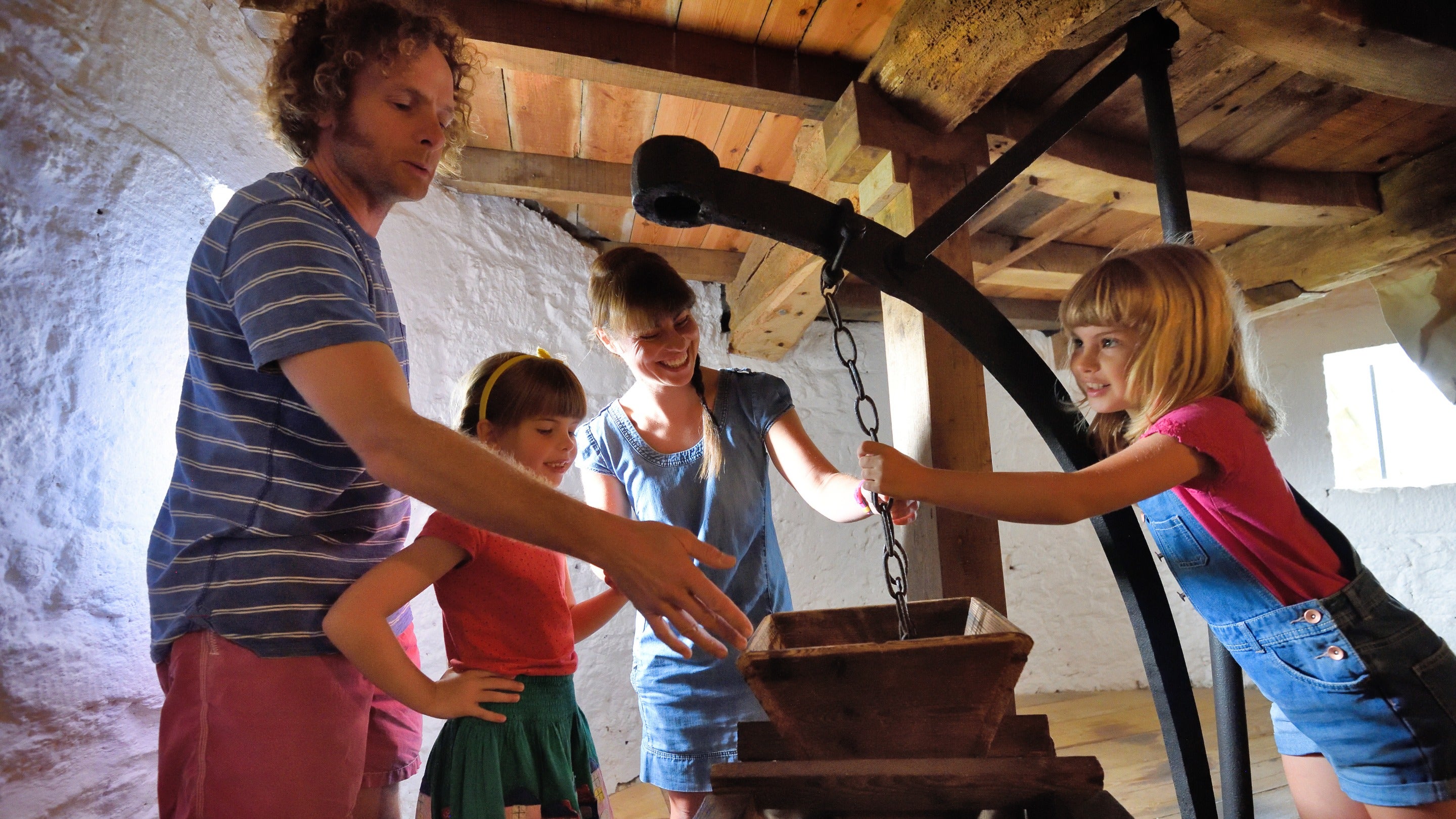 A visiting family touch the machinery inside Bembridge Windmill, Isle of Wight. Built around 1700, it last operated in 1913 but still has most of its original machinery intact