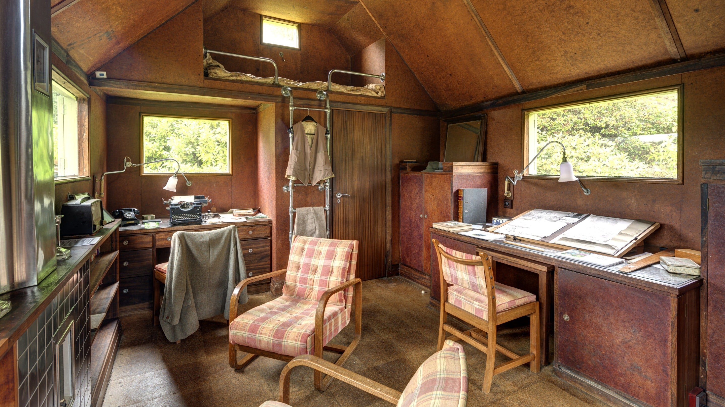 A view inside the single storey wooden building called The Shack at Mottistone Garden and Estate, with wooden in-built furniture, bunk bed and upholstered chairs