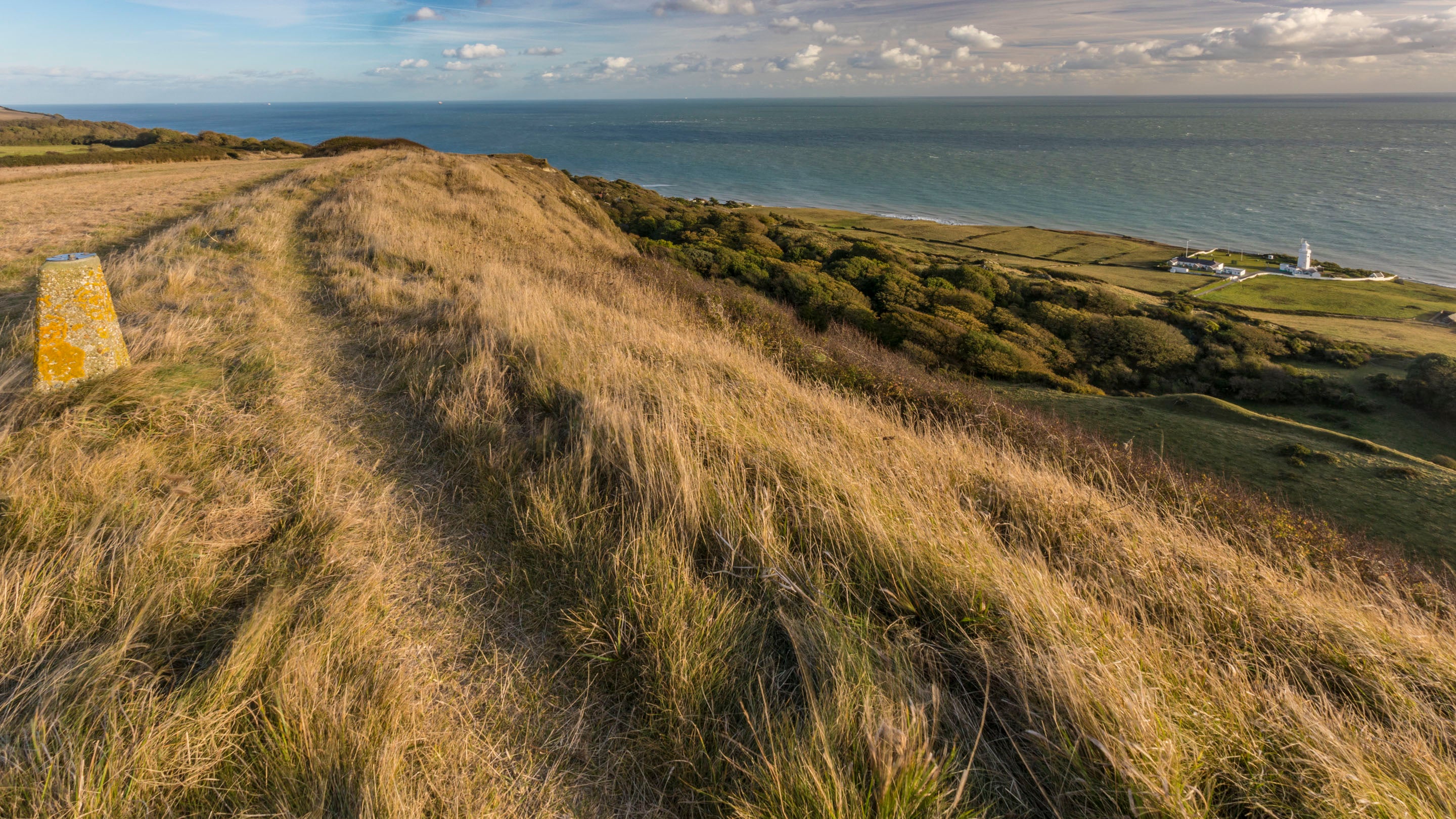 St Catherine's lighthouse seen far below from coast path at the top of Gore Cliff, near a concrete plinth for surveying equipment to check the cliff is not moving