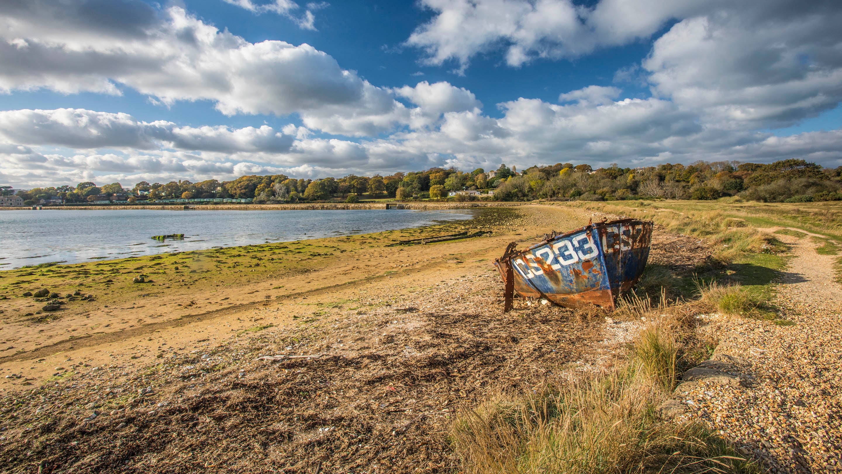 A blue old boat rusts close to the path by the edge of a St Helens Duver lagoon