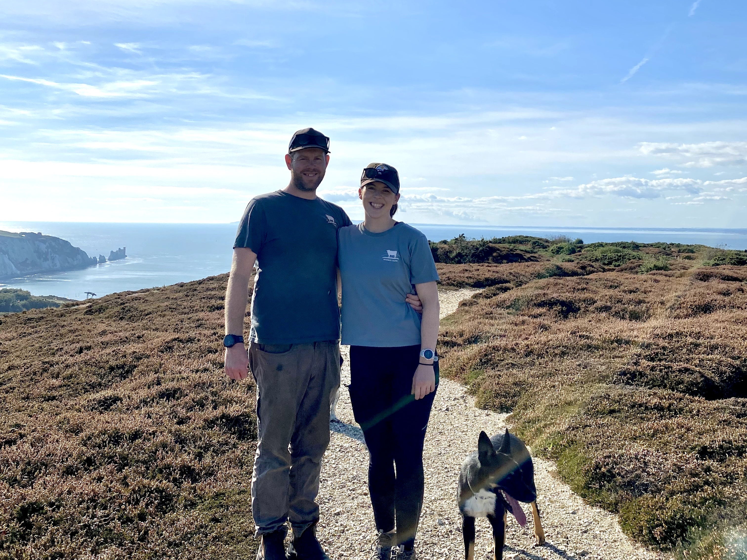 Picture of a man and a woman and a dog on a footpath near some heather with The Needles in the background