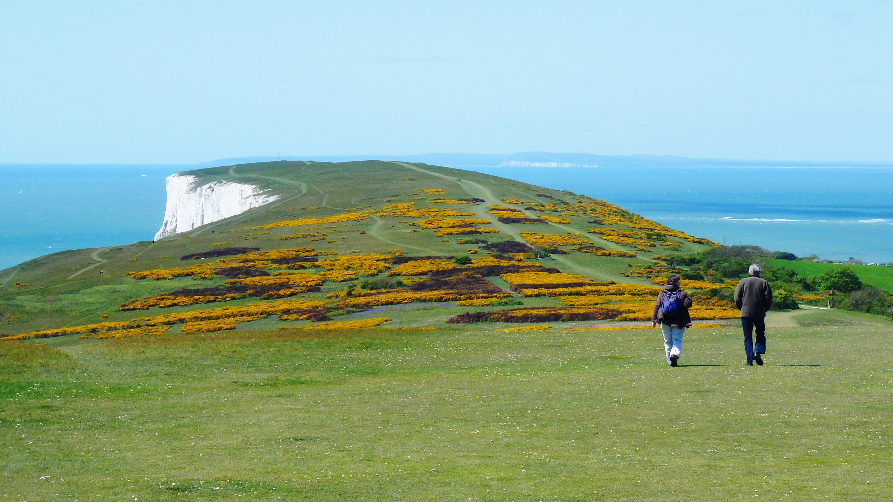 Two walkers setting out along the Needles headland with the white cliffs of Dorset visible over the sea