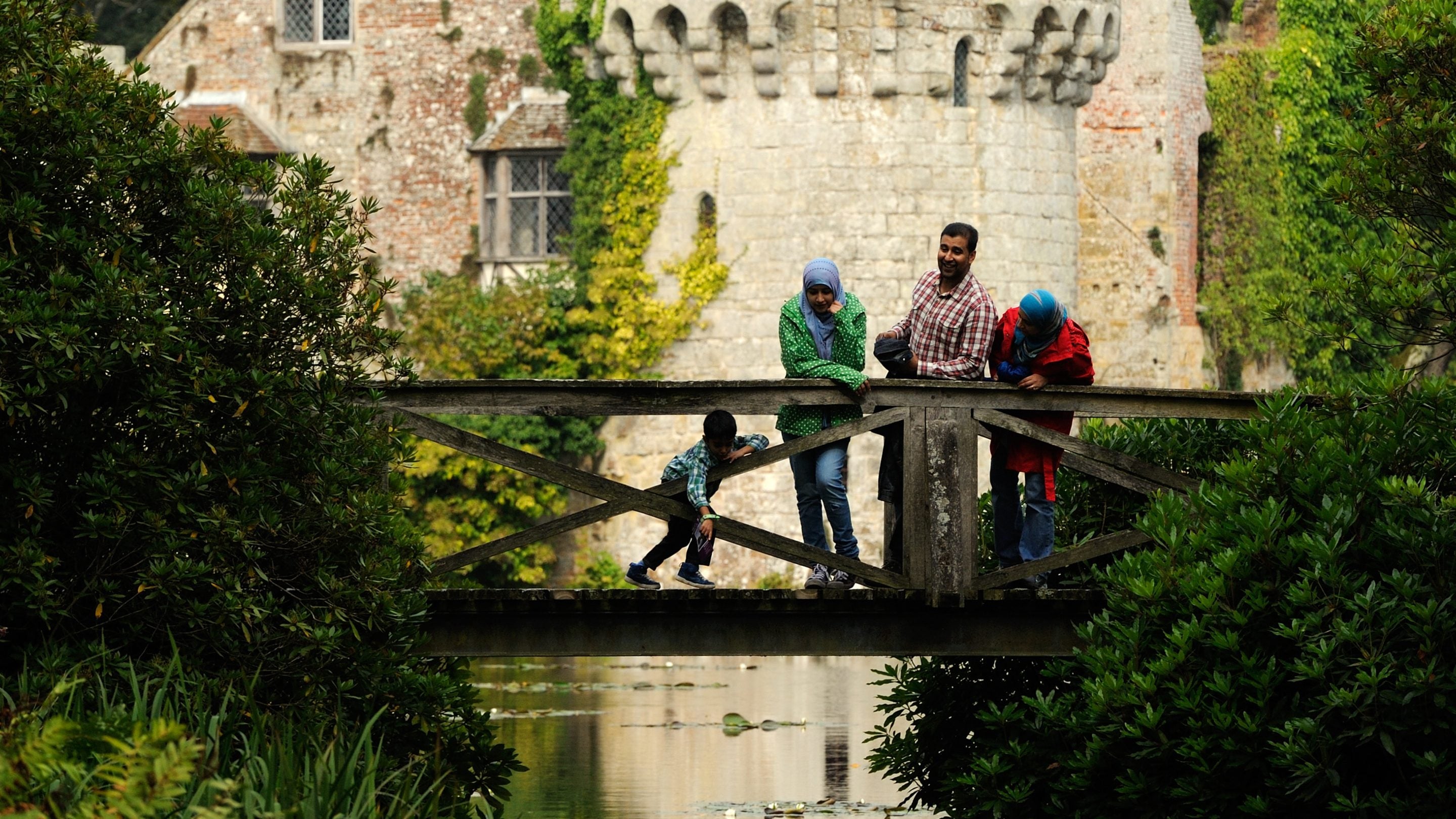 Family on a bridge over the moat at Scotney Castle, Kent. A young child is pointing at something in the water below.