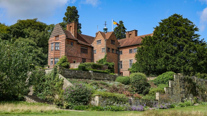 A view of the red bricked house at Chartwell with terraced gardens below and a blue sky above