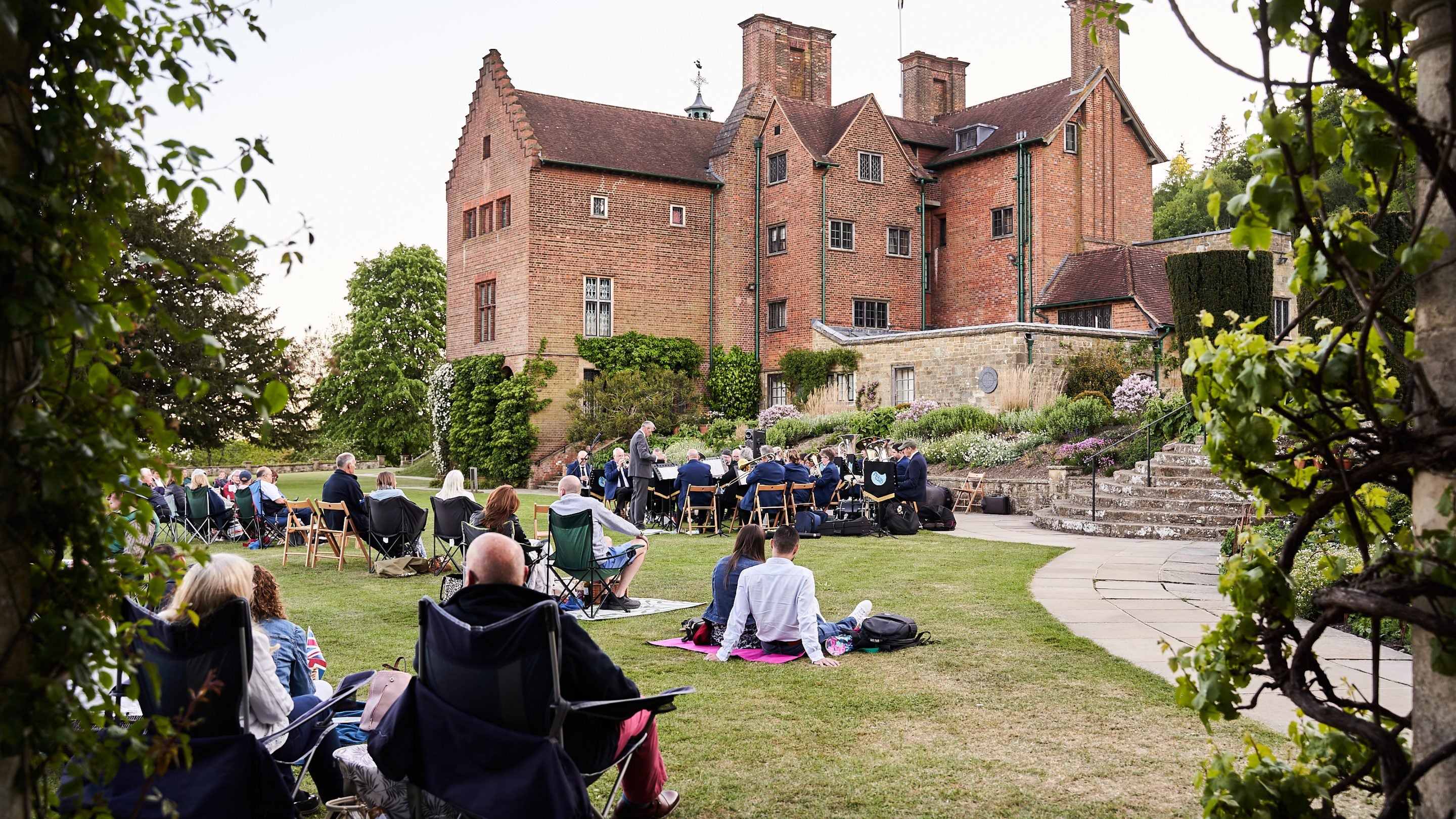 People picnicking on the lawn while a concert band plays in front of the house at Chartwell.