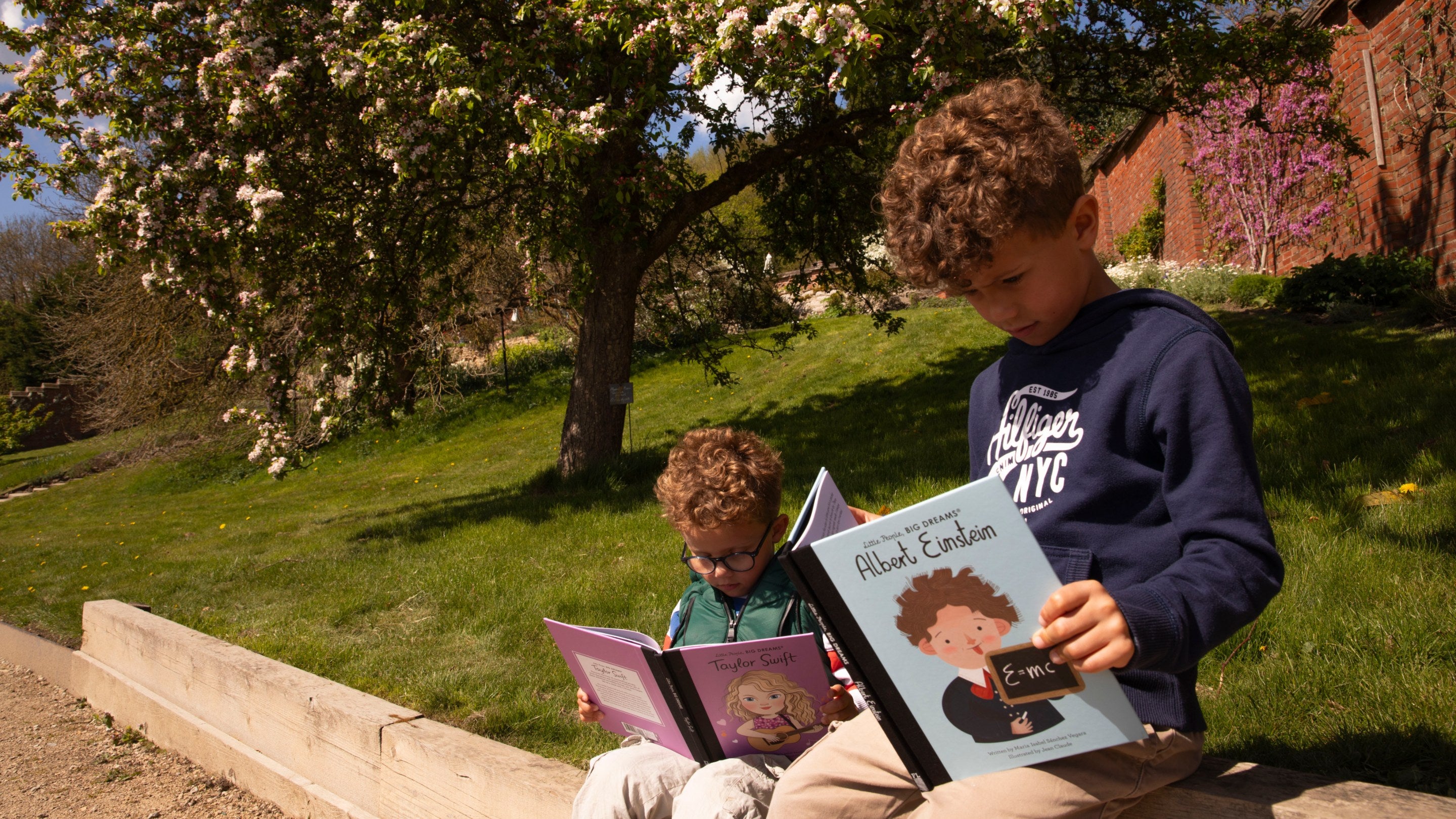 Children reading the Little People BIG DREAMS books at Chartwell beside an apple blossom tree.