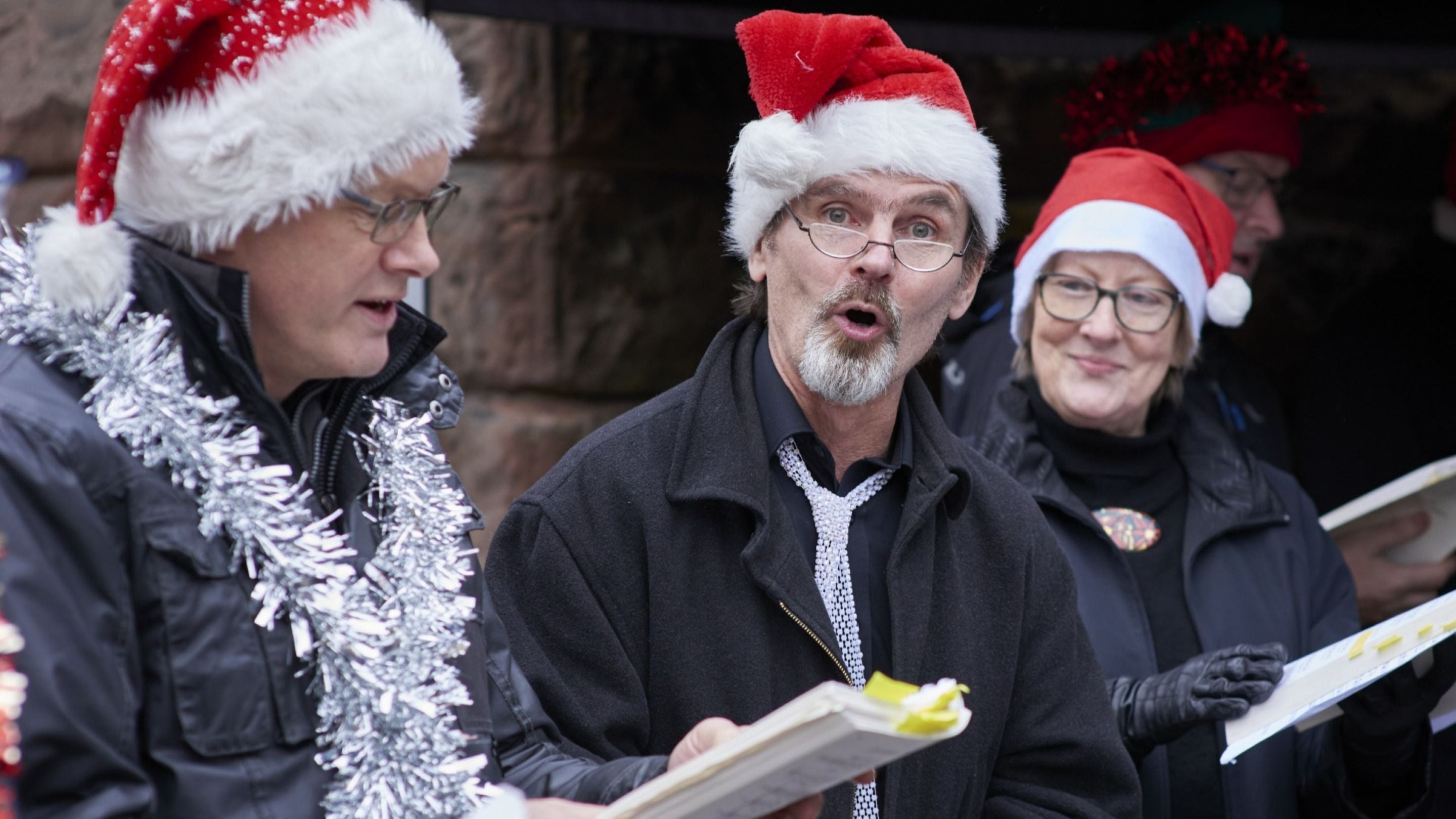 Carol singers in Santa hats holding sheet music