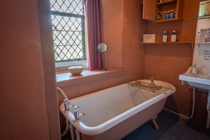 White and pink bath in front of a window in a bathroom with walls painted in a terracotta colour.