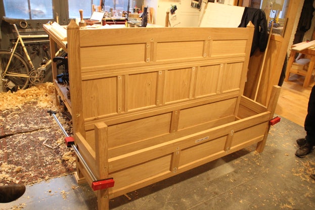 A large wooden bench located in a workshop with tools around it and sawdust on the floor.