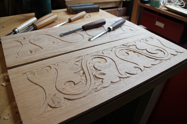 A pattern with swirls and waves carved into a piece of wood, with carving tools laying on top of the piece of wood.