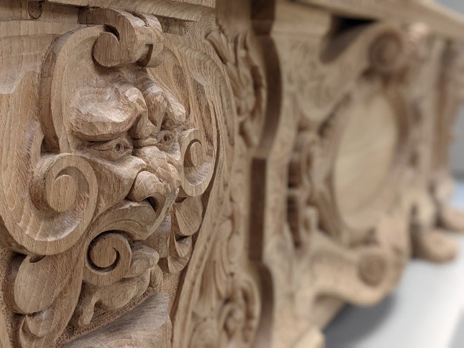 A close up of a carved face on a large piece of wooden furniture.