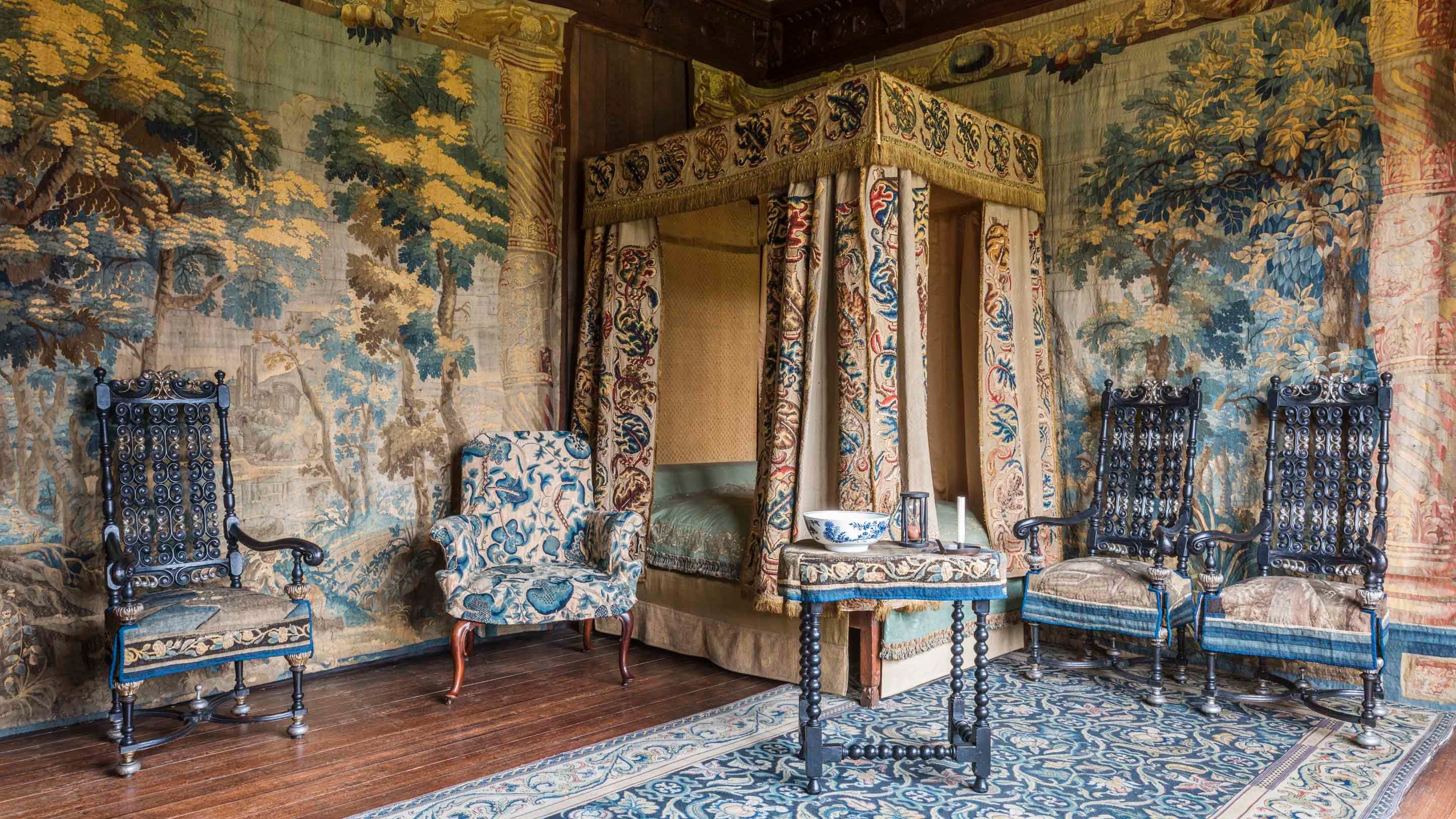 A lavishly decorated bedroom with a four poster bed hung with embroidered hangings and tapestry hung walls at Knole in Kent