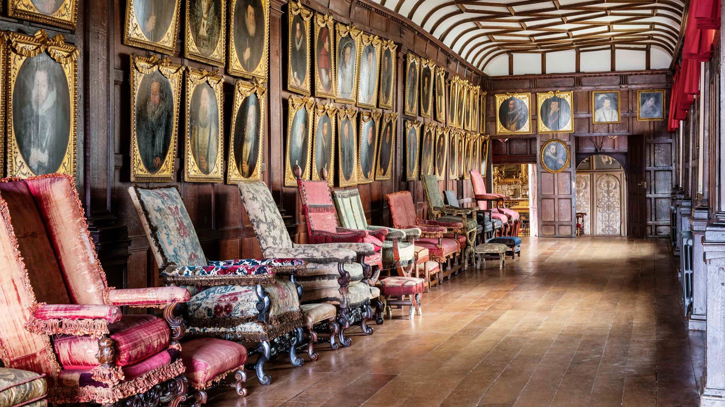 The wood panelled Brown Gallery at Knole in Kent, lined with rows of 16th and 17th century gold framed oil portraits and a collection of early English furniture set in a row underneath