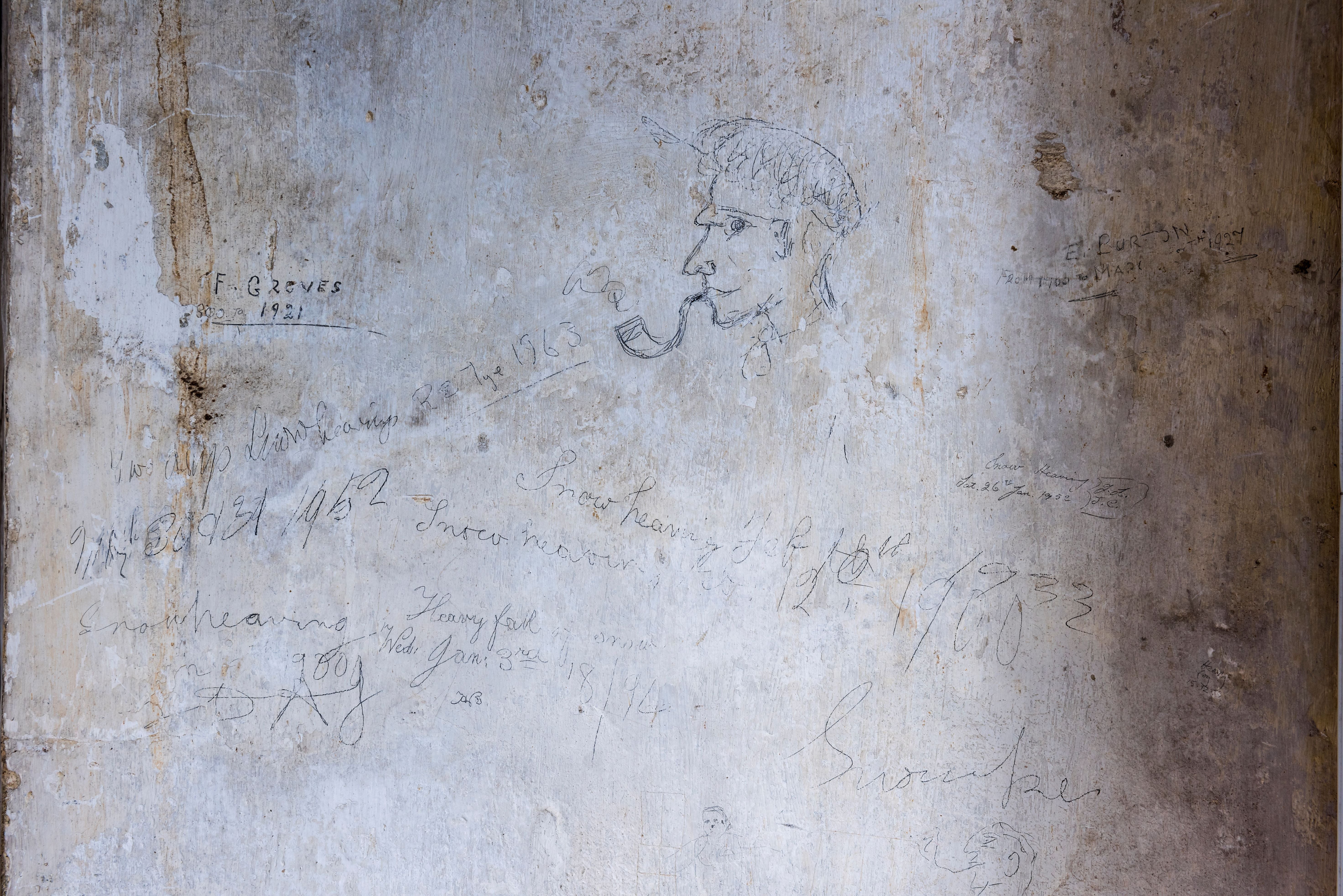 writing and a drawing of a man smoking a pipe on a grey wall