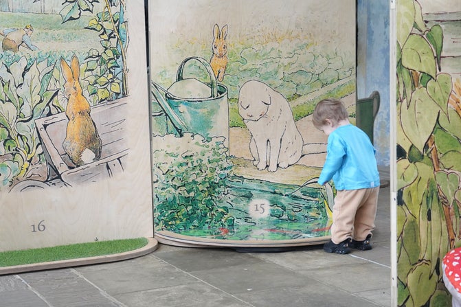 A small child is looking into a mirror that has an illustrated board above it with a white cat, a brown rabbit, a watering can and plants on.