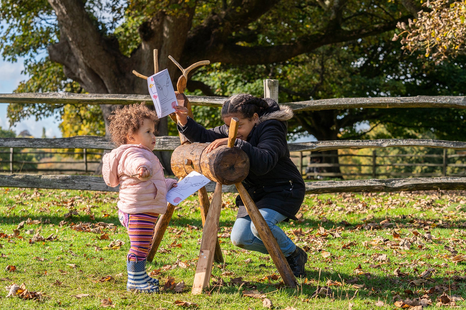 Children taking part in deer trail at Knole standing next to wooden deer