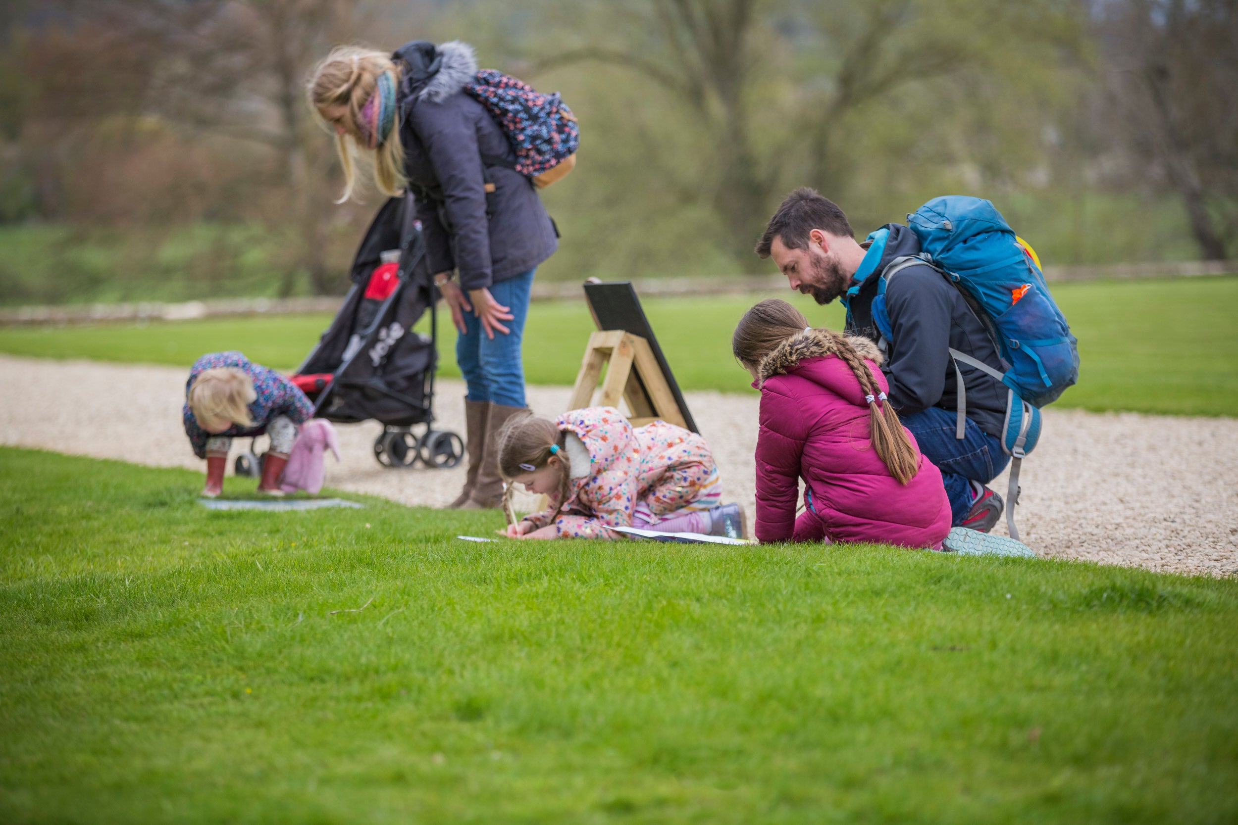 Family gathered around a trail point with children leaning on grass.
